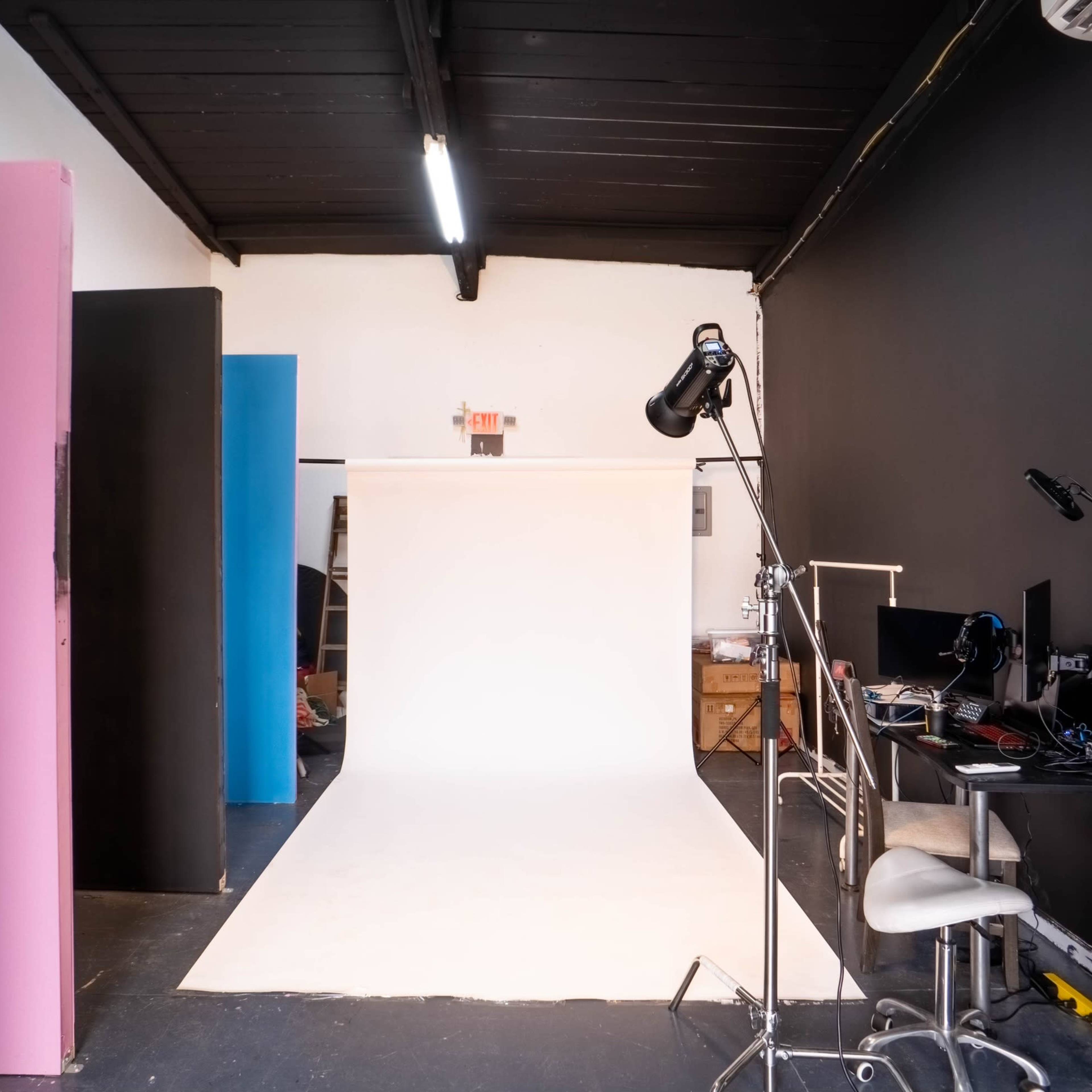 A photography studio with a white backdrop, colorful vertical panels, and a desk set up with computers.