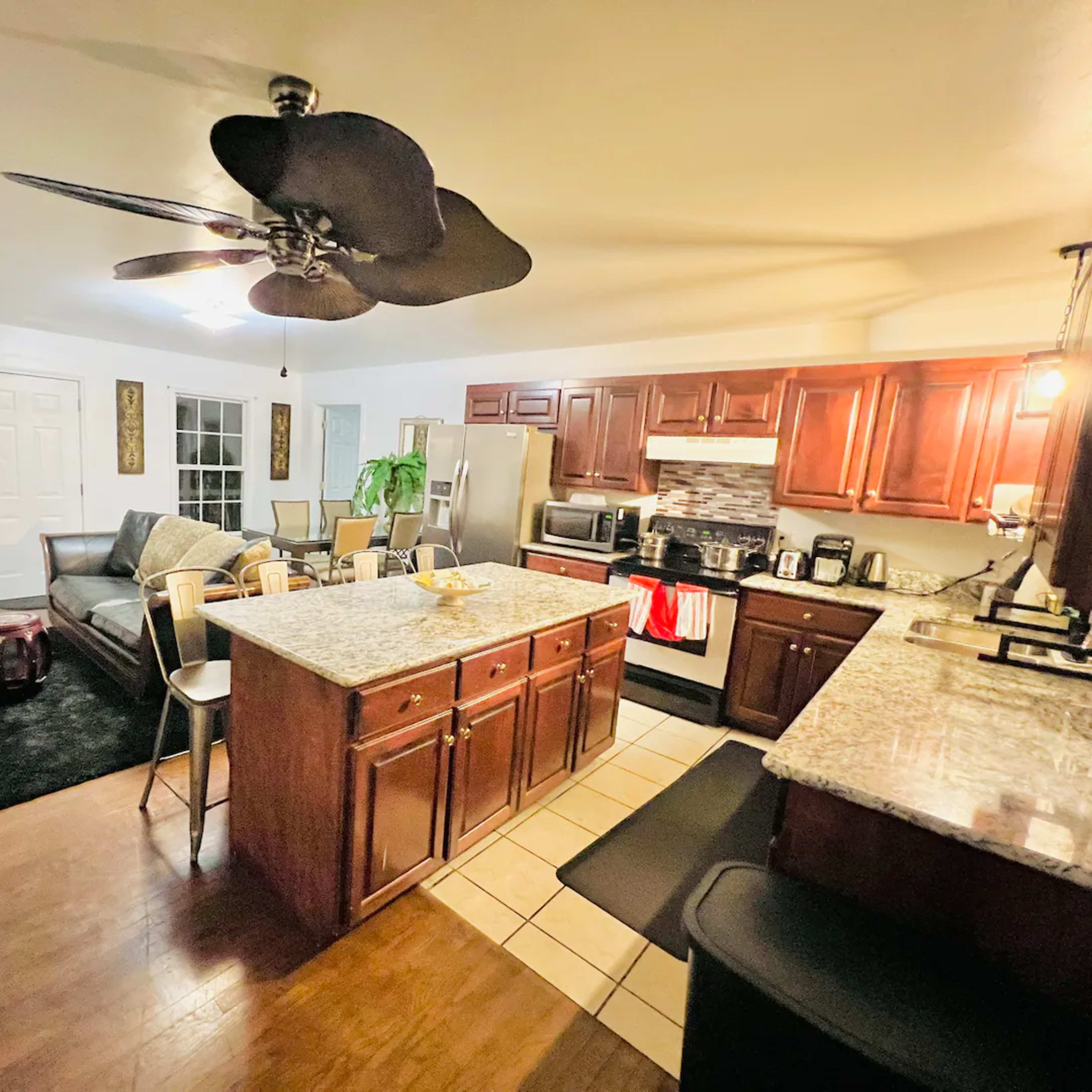 A modern kitchen and living area with wooden cabinets, a granite island, and a seating area with a sofa.