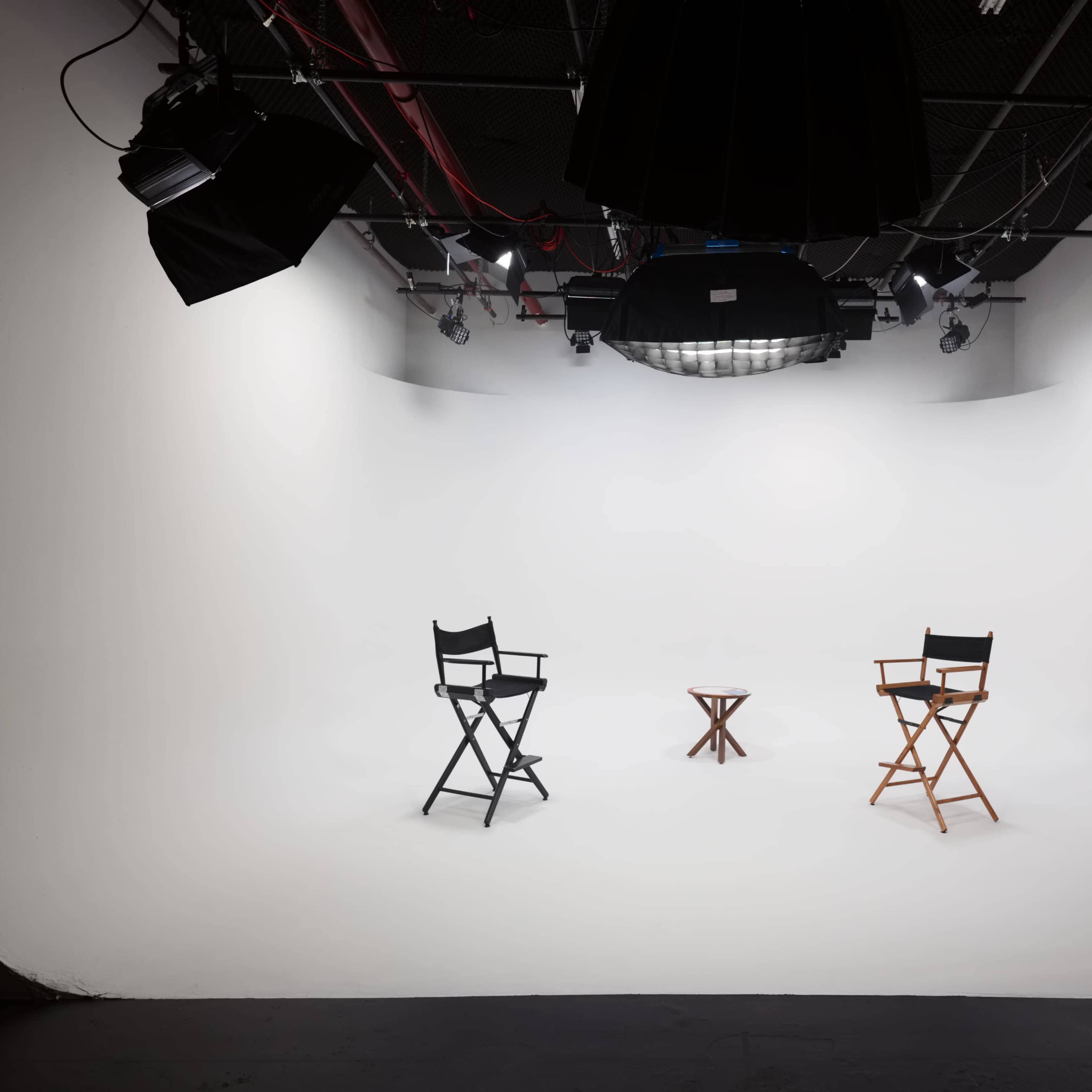 A minimalist set featuring two director's chairs and a small table on a white backdrop.
