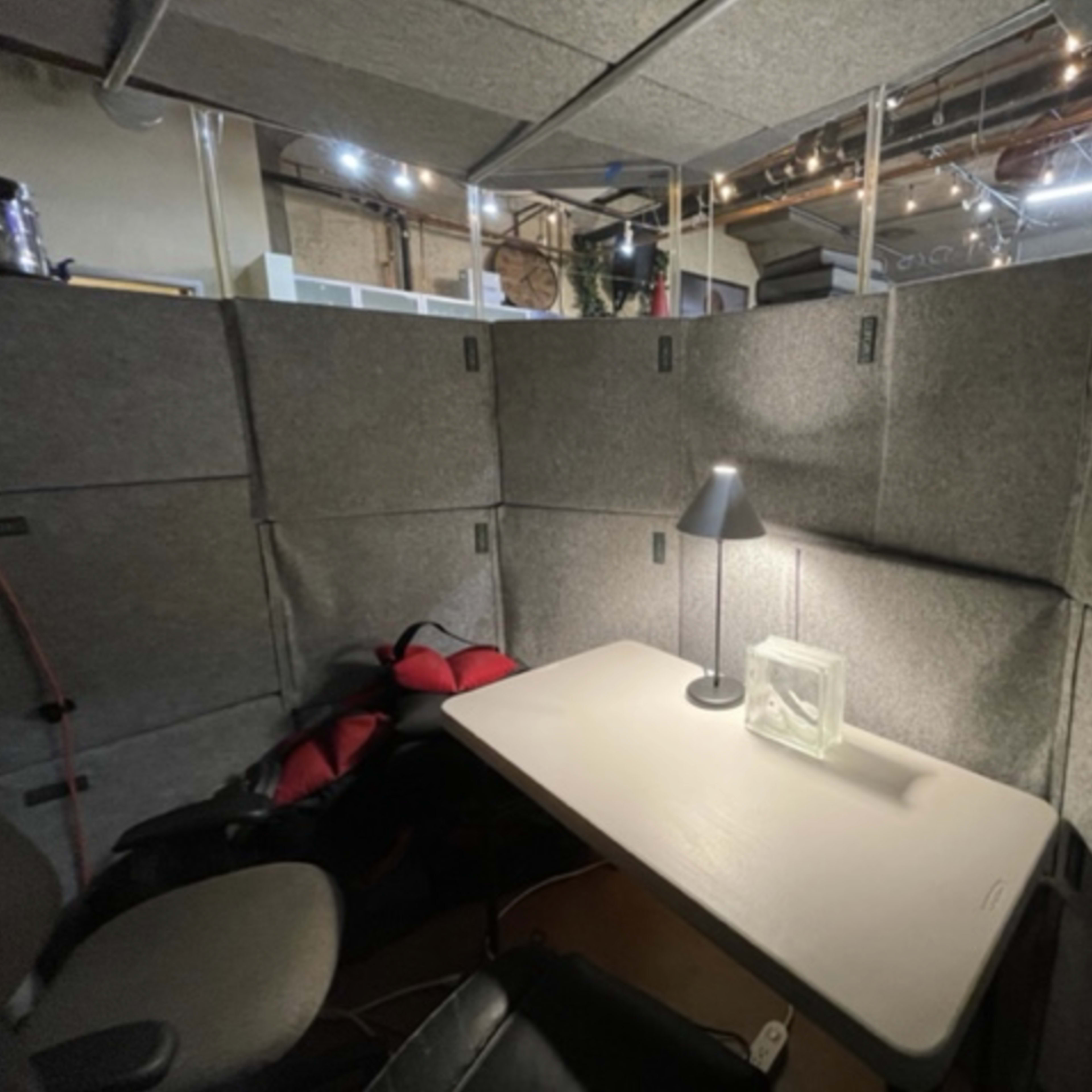 A small workspace is enclosed by gray acoustic panels, featuring a desk with a lamp and a decorative box.