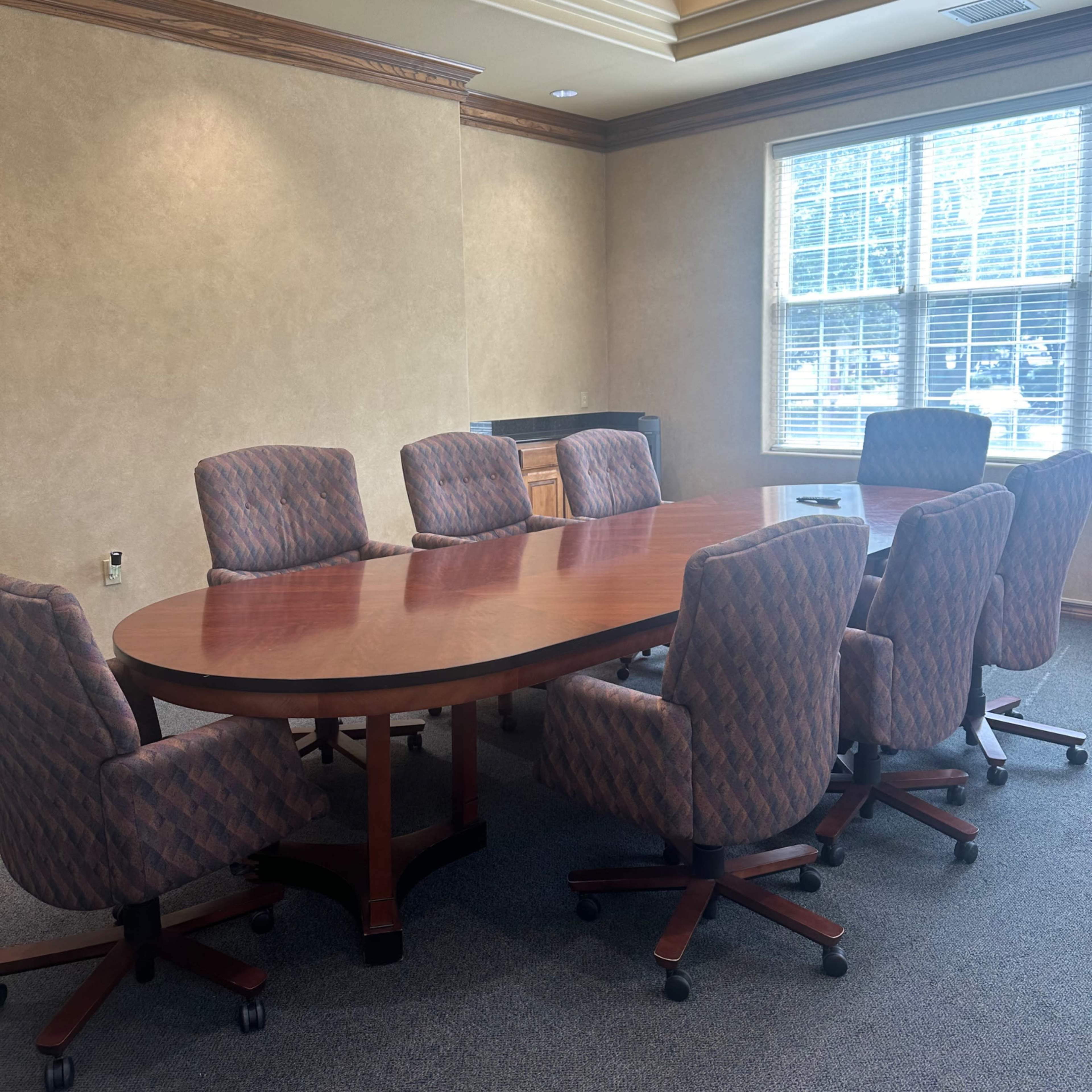 A conference room with a large oval wooden table surrounded by eight upholstered chairs.
