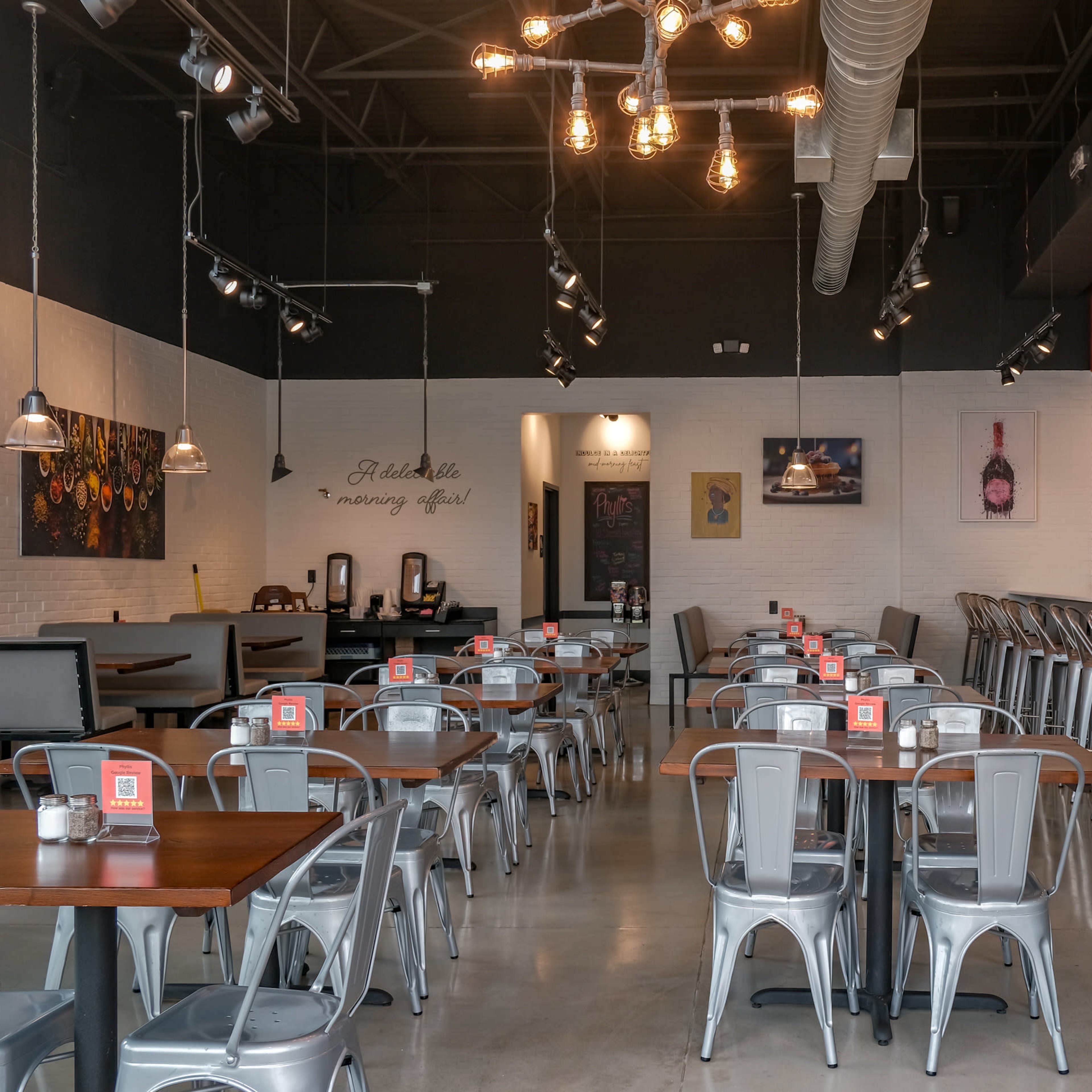 A modern restaurant interior with metal chairs and tables, featuring a bar area and decorative wall art.