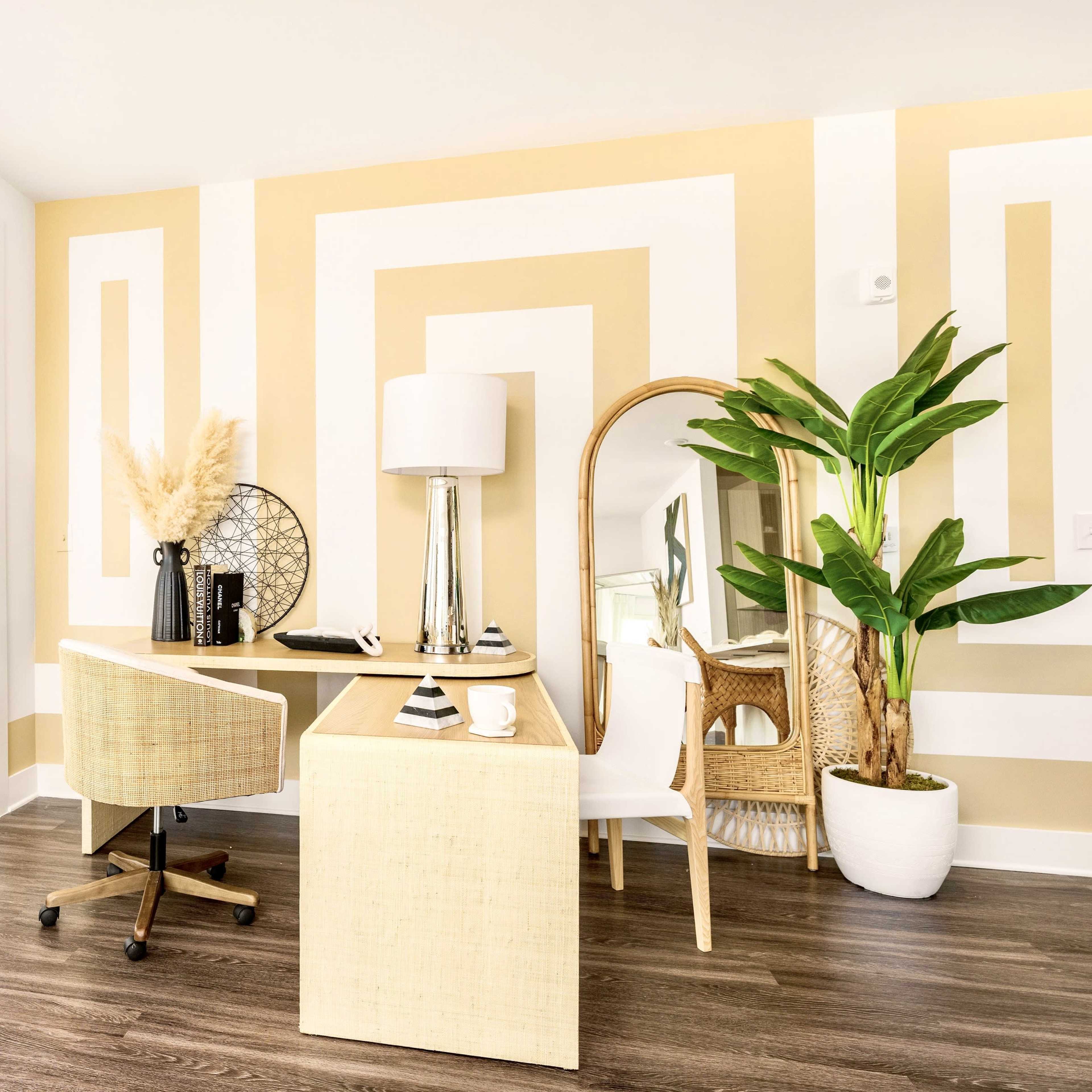 A bright home office with a desk, a chair, and large windows featuring patterned walls in yellow and white.