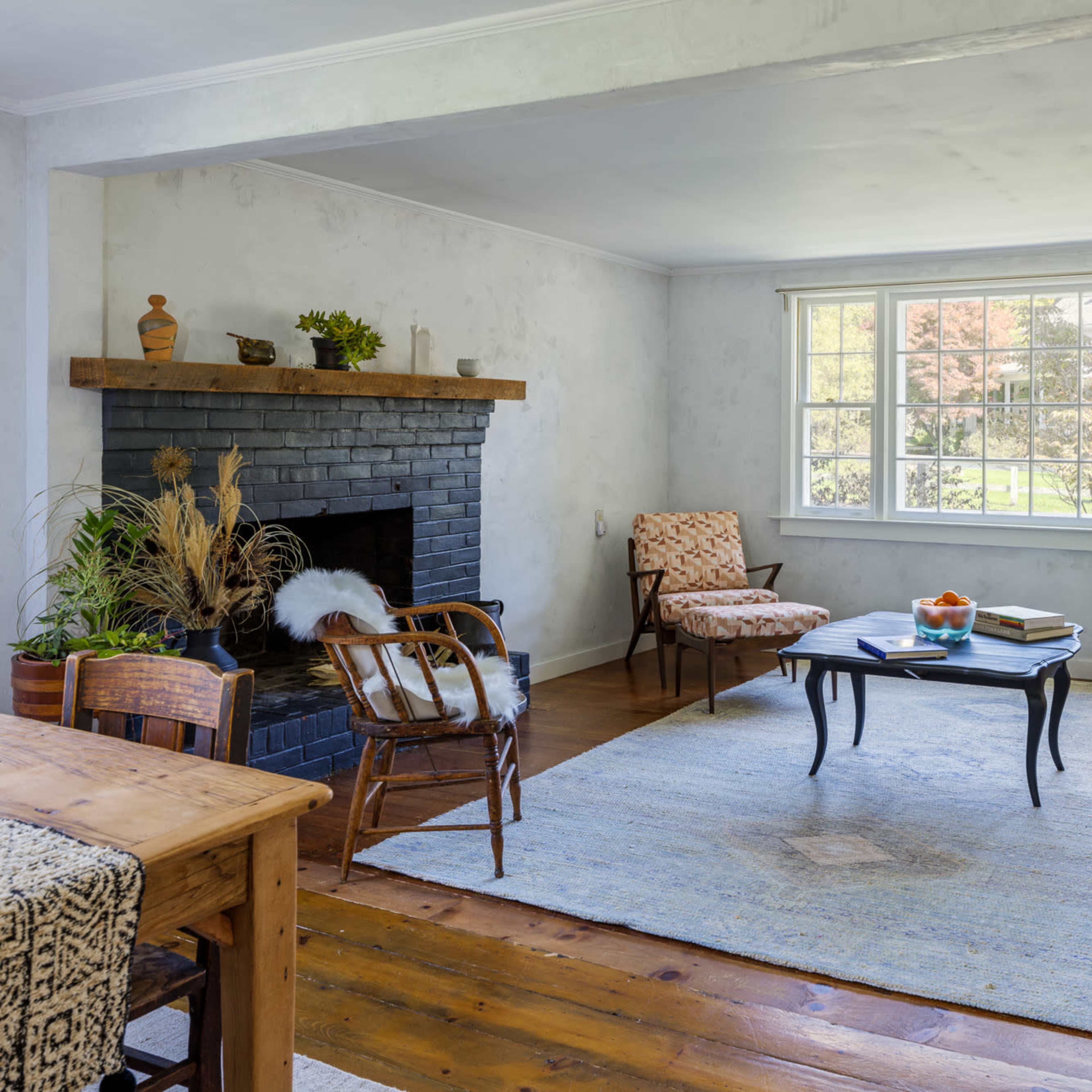 A living room features a sofa, two armchairs, a coffee table, and a fireplace, with large windows allowing natural light to enter.