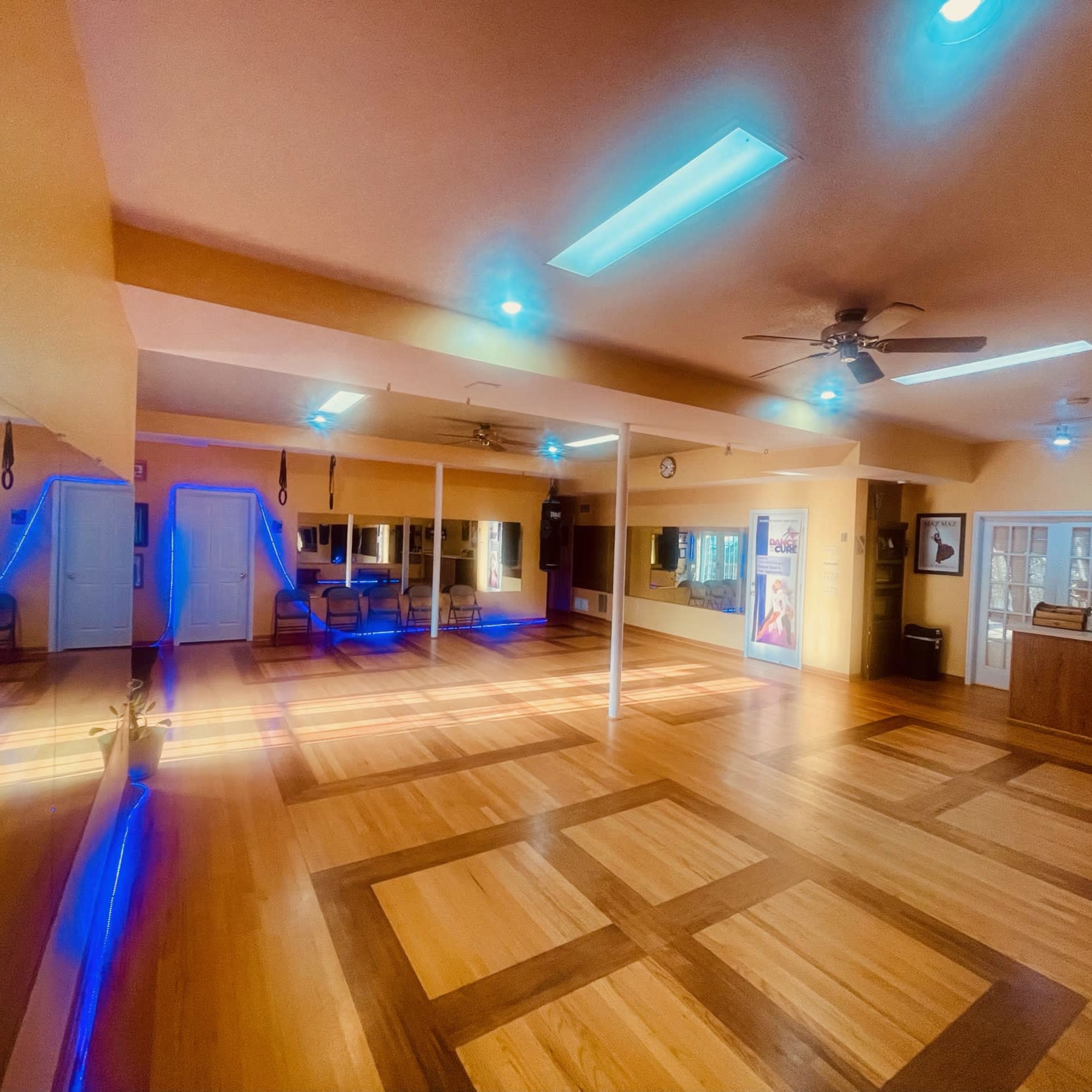 An empty dance studio with wooden floors, ceiling fans, and mirrors lining the walls.