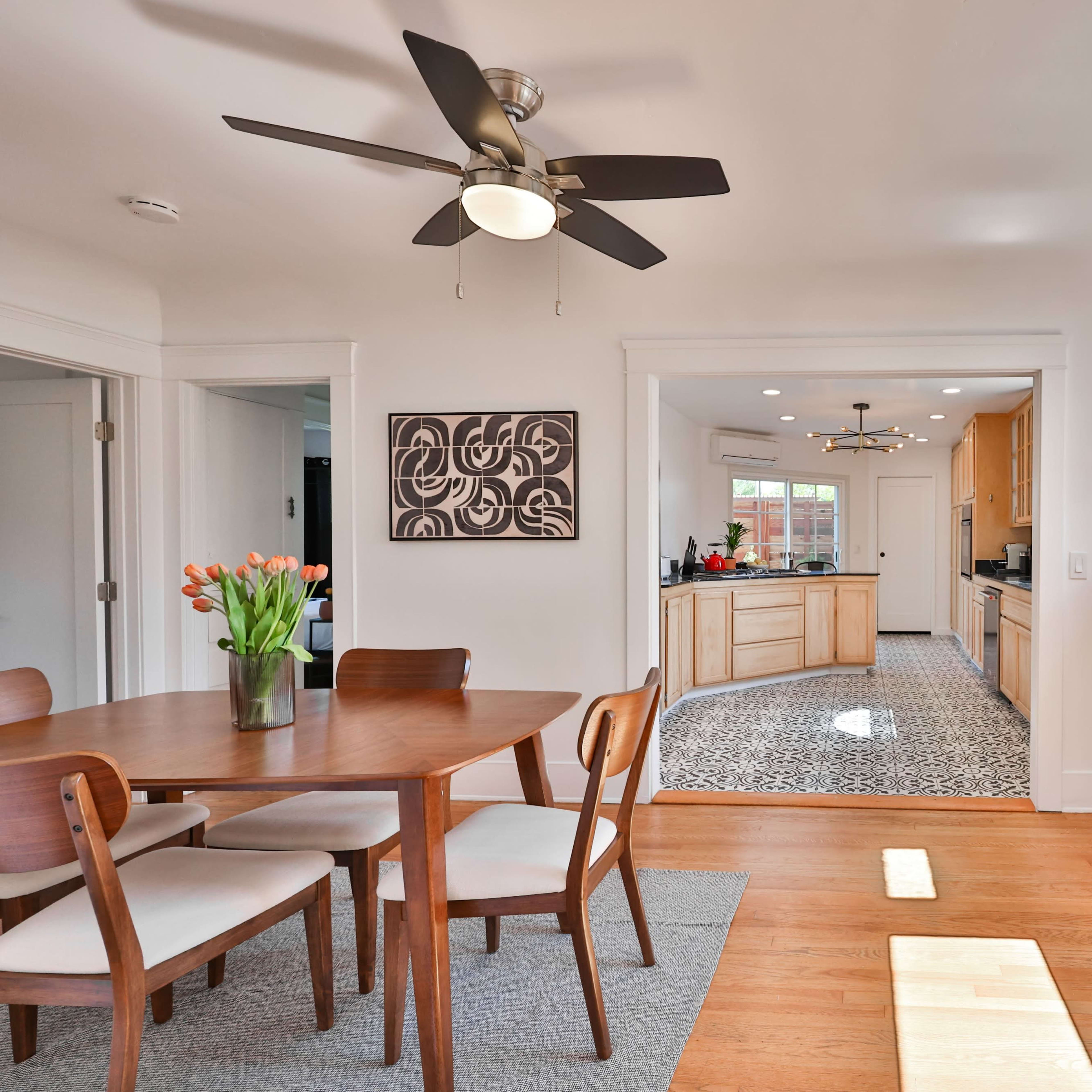 A dining area with a circular table and chairs leads into a kitchen with wooden cabinetry and a patterned floor.