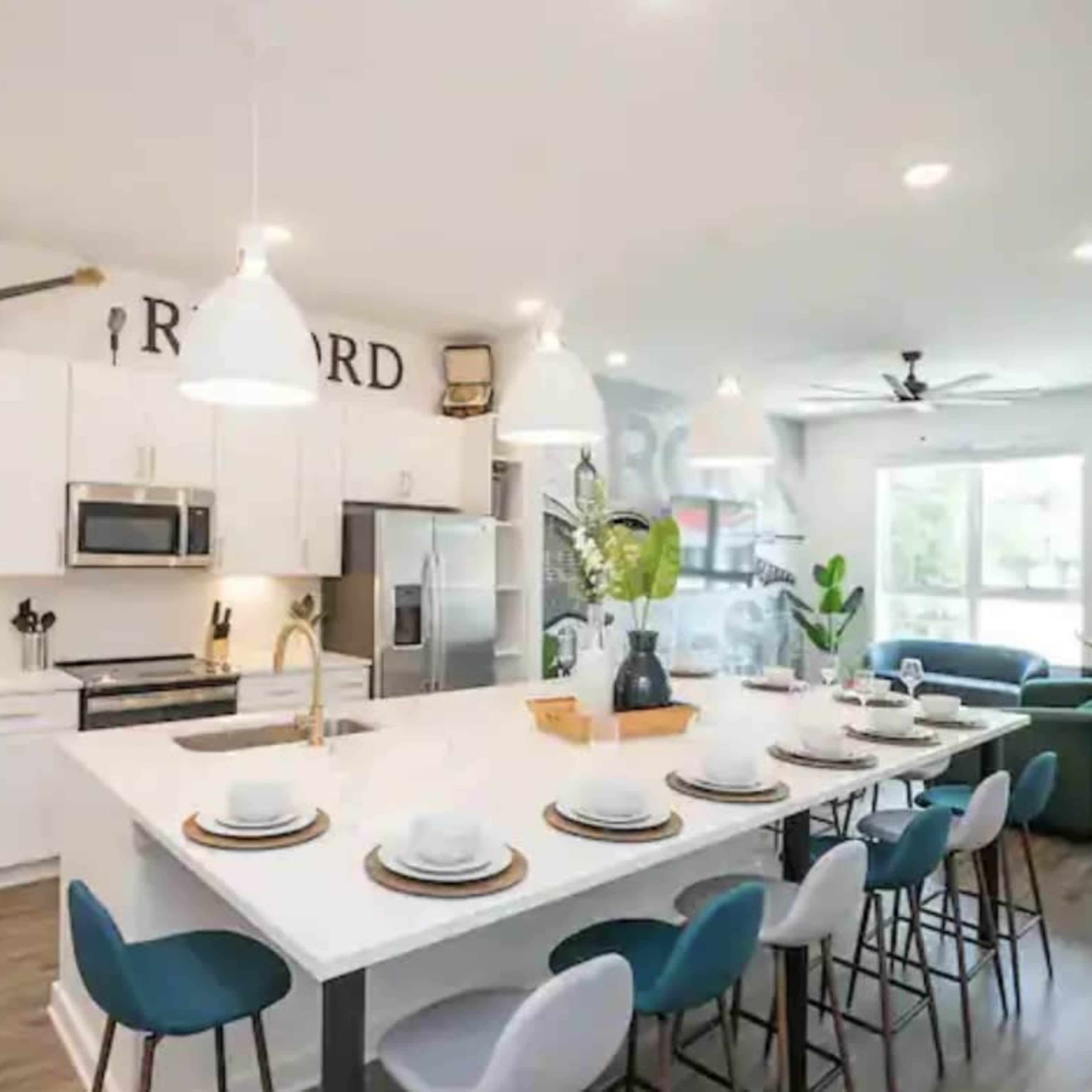A modern kitchen with a large island, white cabinetry, stainless steel appliances, and a dining area set for eight people.