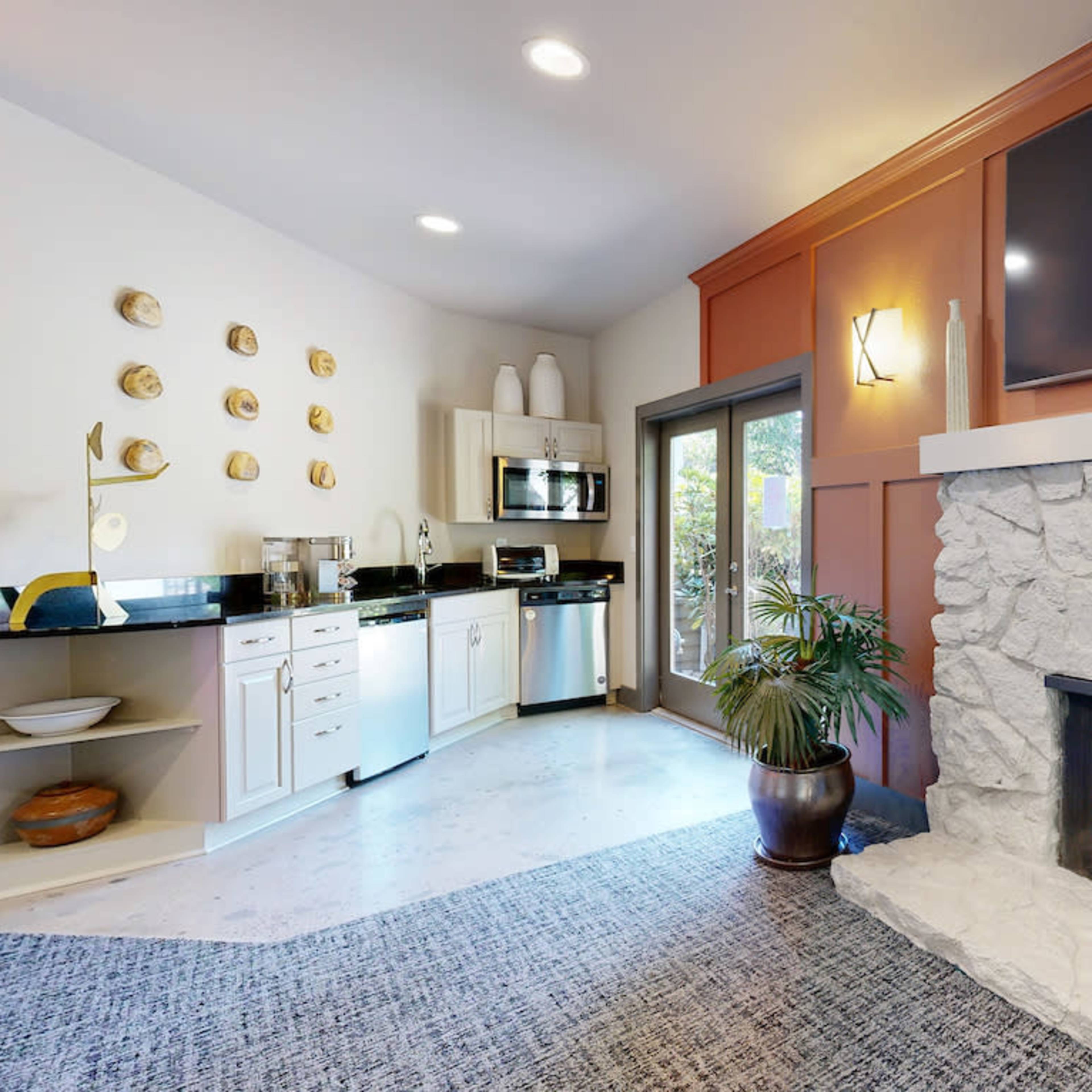 A modern living area with a stone fireplace, a kitchen area, and large windows leading to an outdoor space.