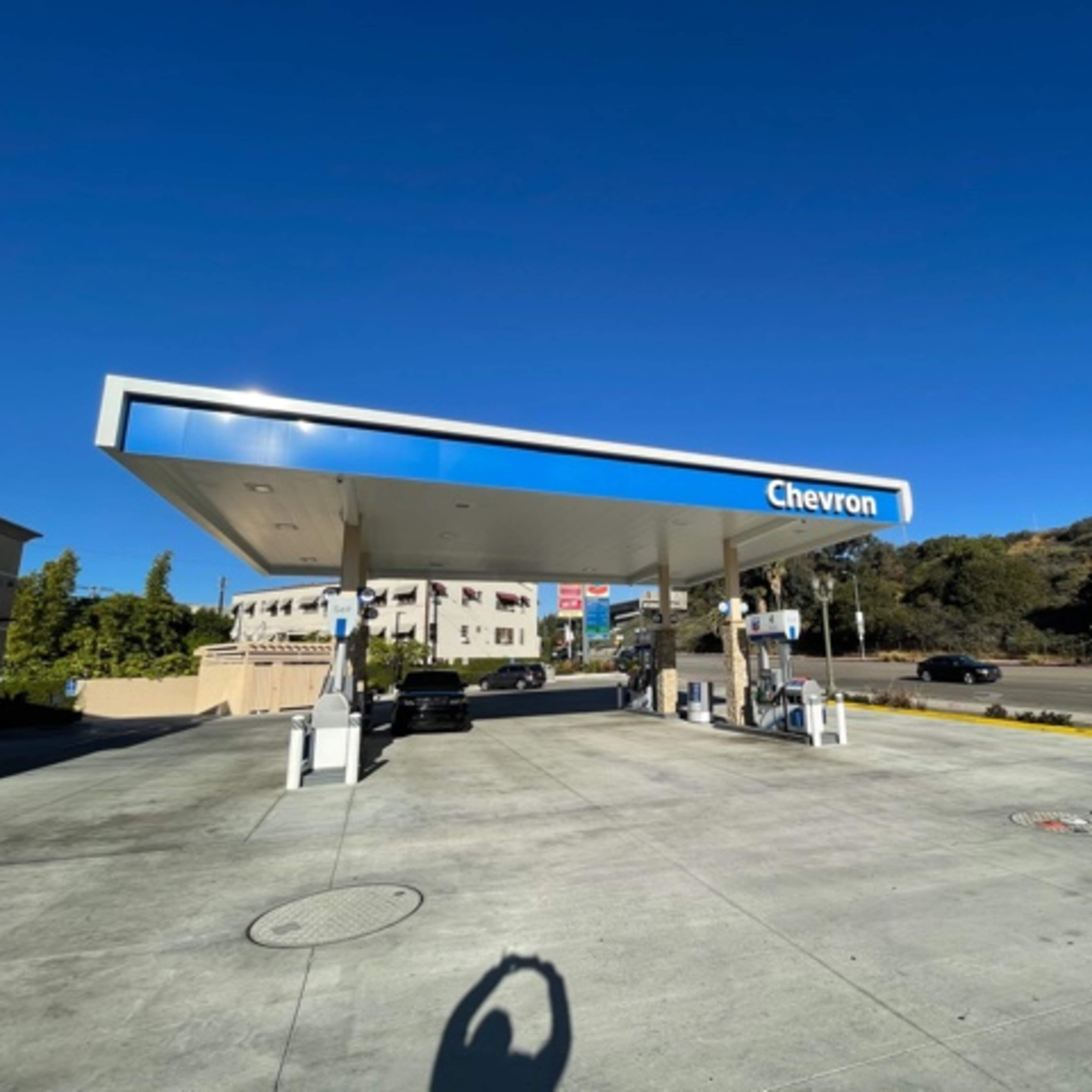 A Chevron gas station with a clear blue sky and hills in the background is shown.