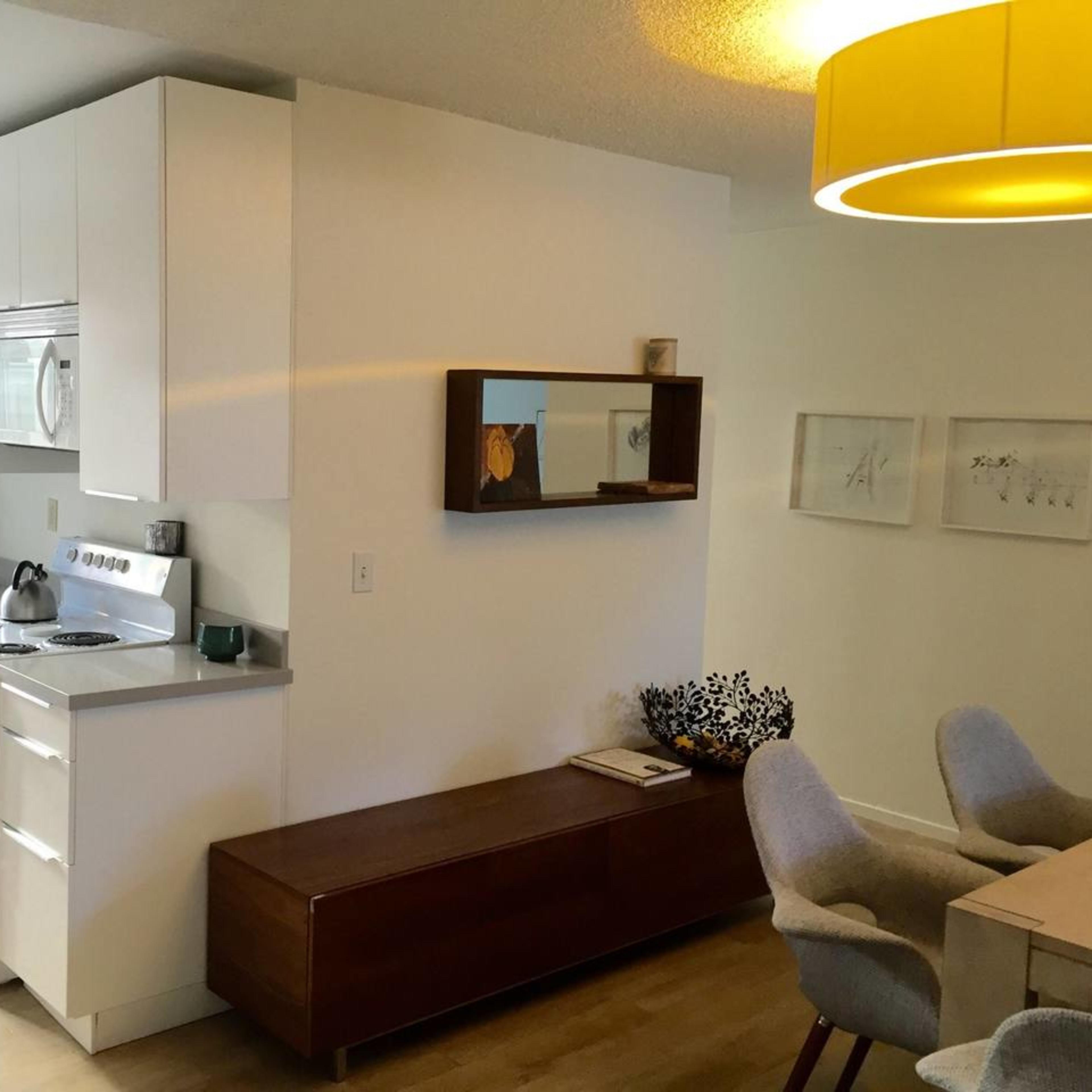 A modern kitchen area with white cabinetry, a stainless steel stove, and a wooden sideboard, adjacent to a dining space with grey chairs and a pendant light.
