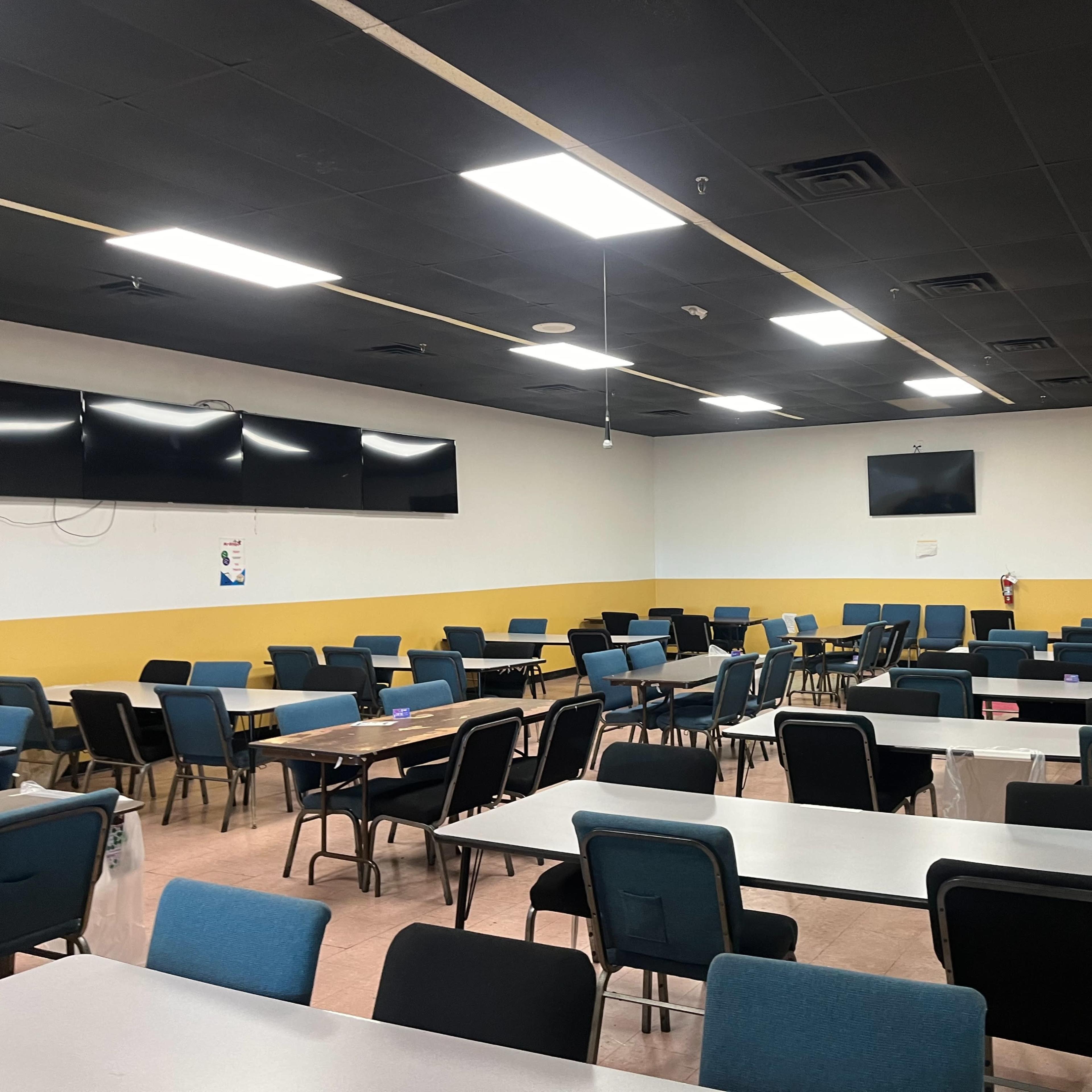 A spacious dining area with rows of tables and chairs, and several wall-mounted televisions.
