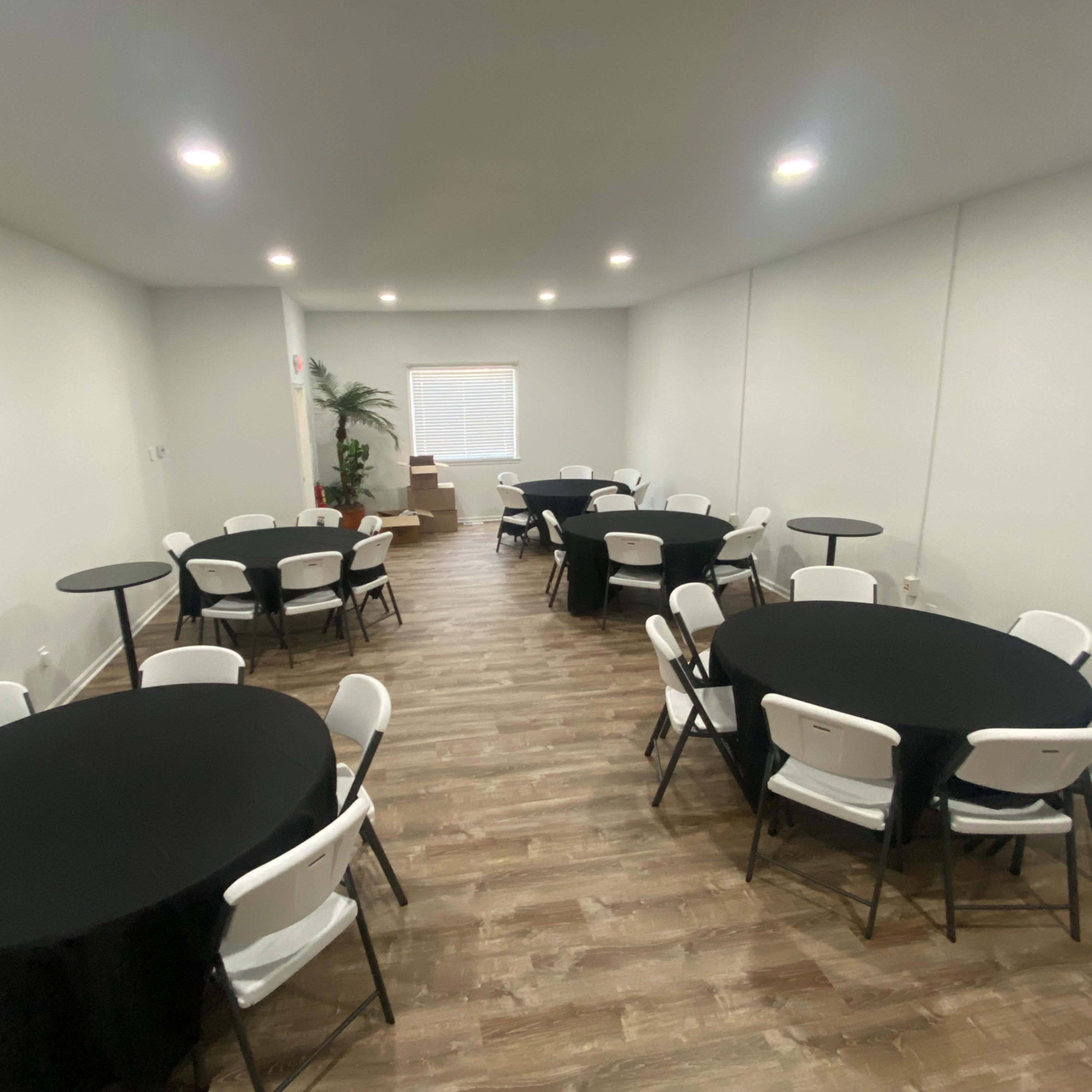 A spacious room with multiple round tables covered in black tablecloths and equipped with white chairs.