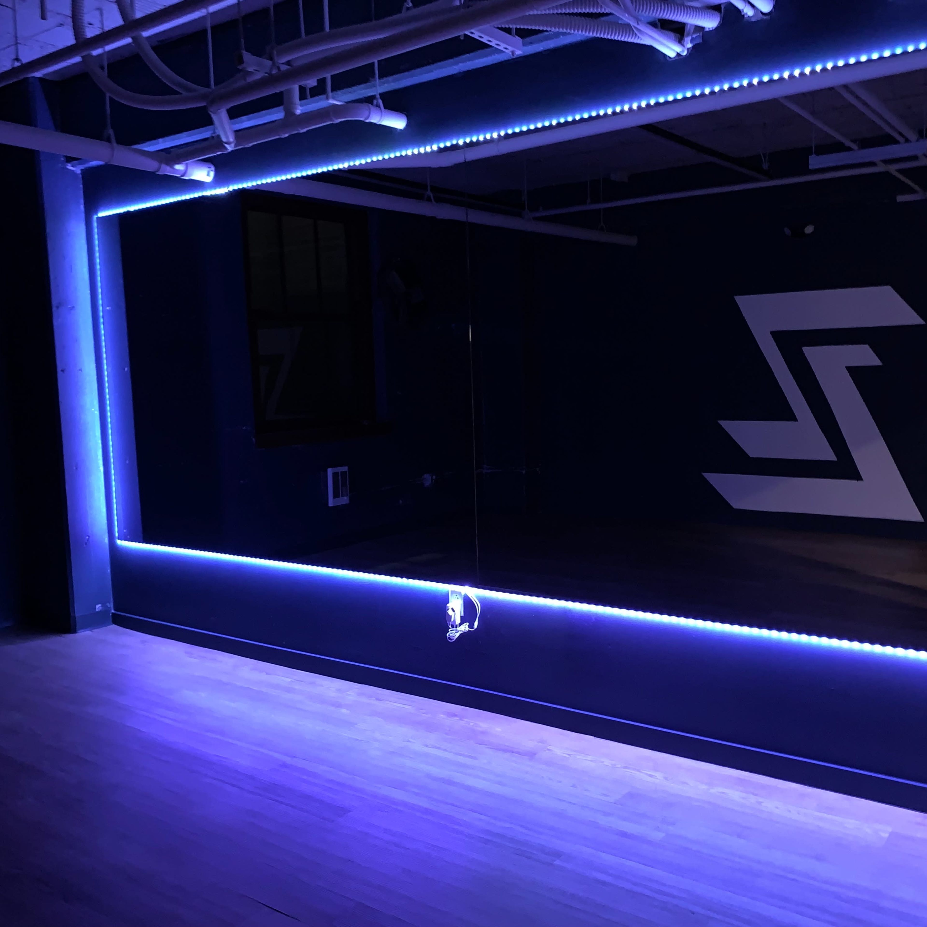 A dimly lit room with a large mirror framed by blue LED lights and a geometric design on the wall.