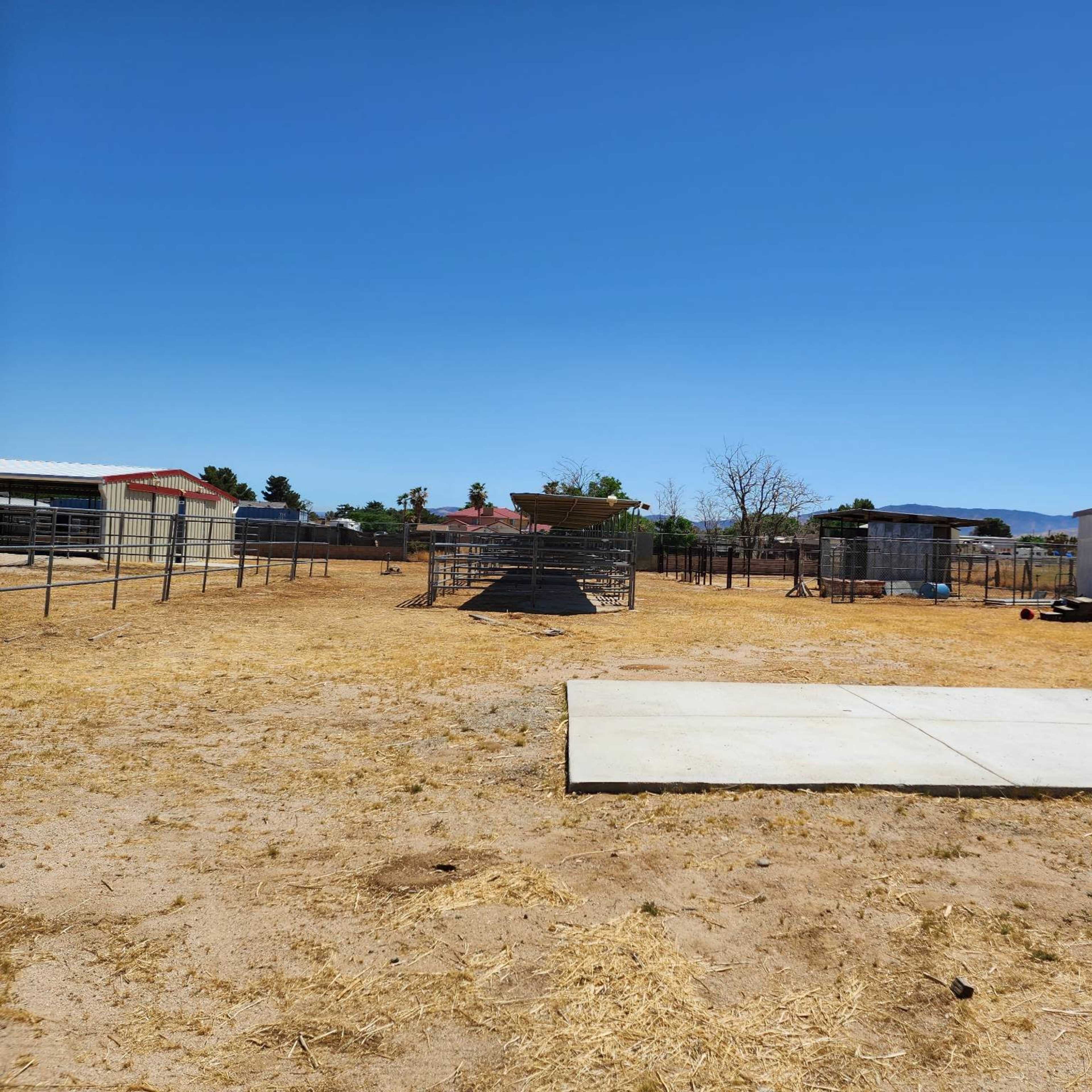An open, dry landscape with fences, enclosures, and storage structures under a clear blue sky.