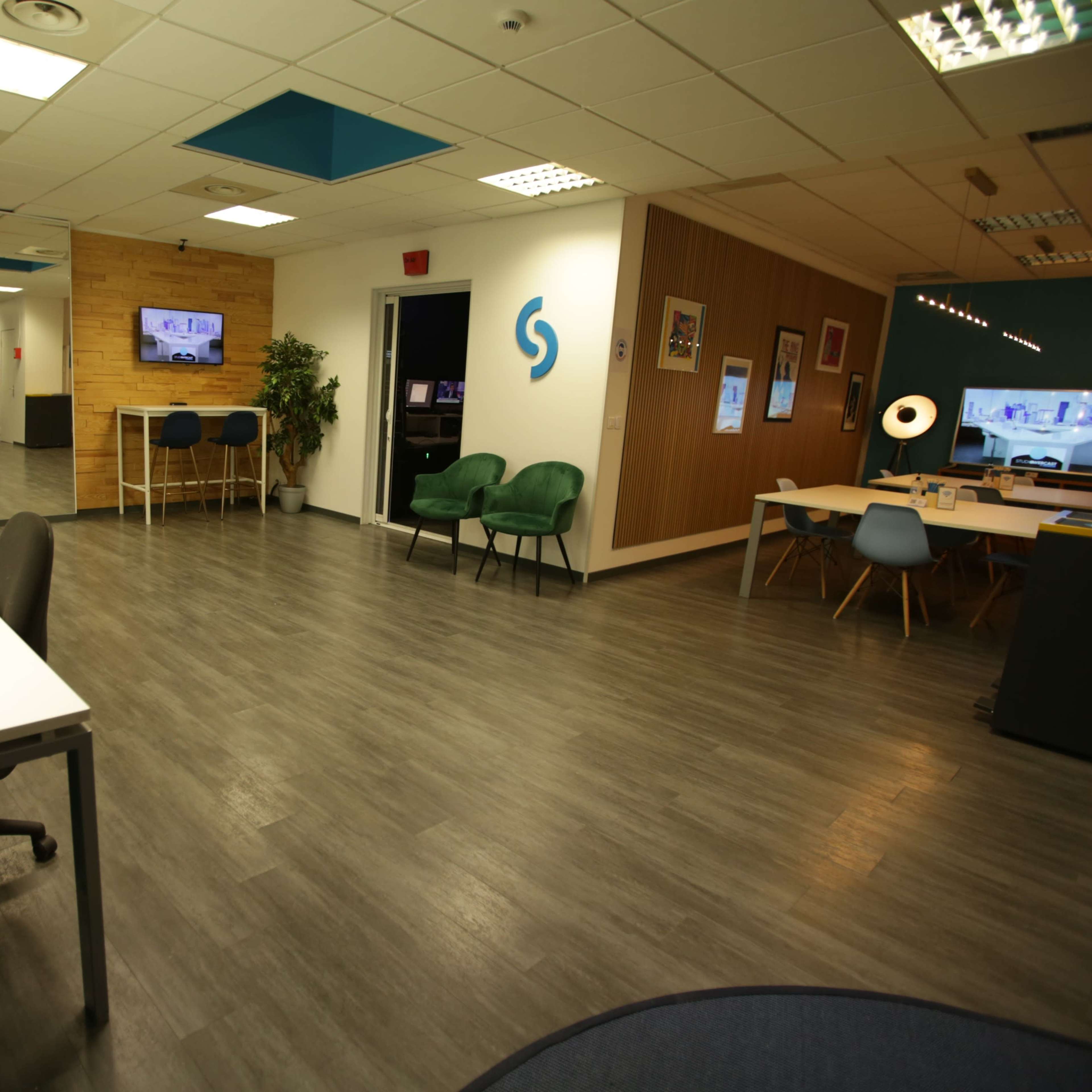 A modern office space with multiple stations, including desks, seating areas, and a TV screen on the walls.