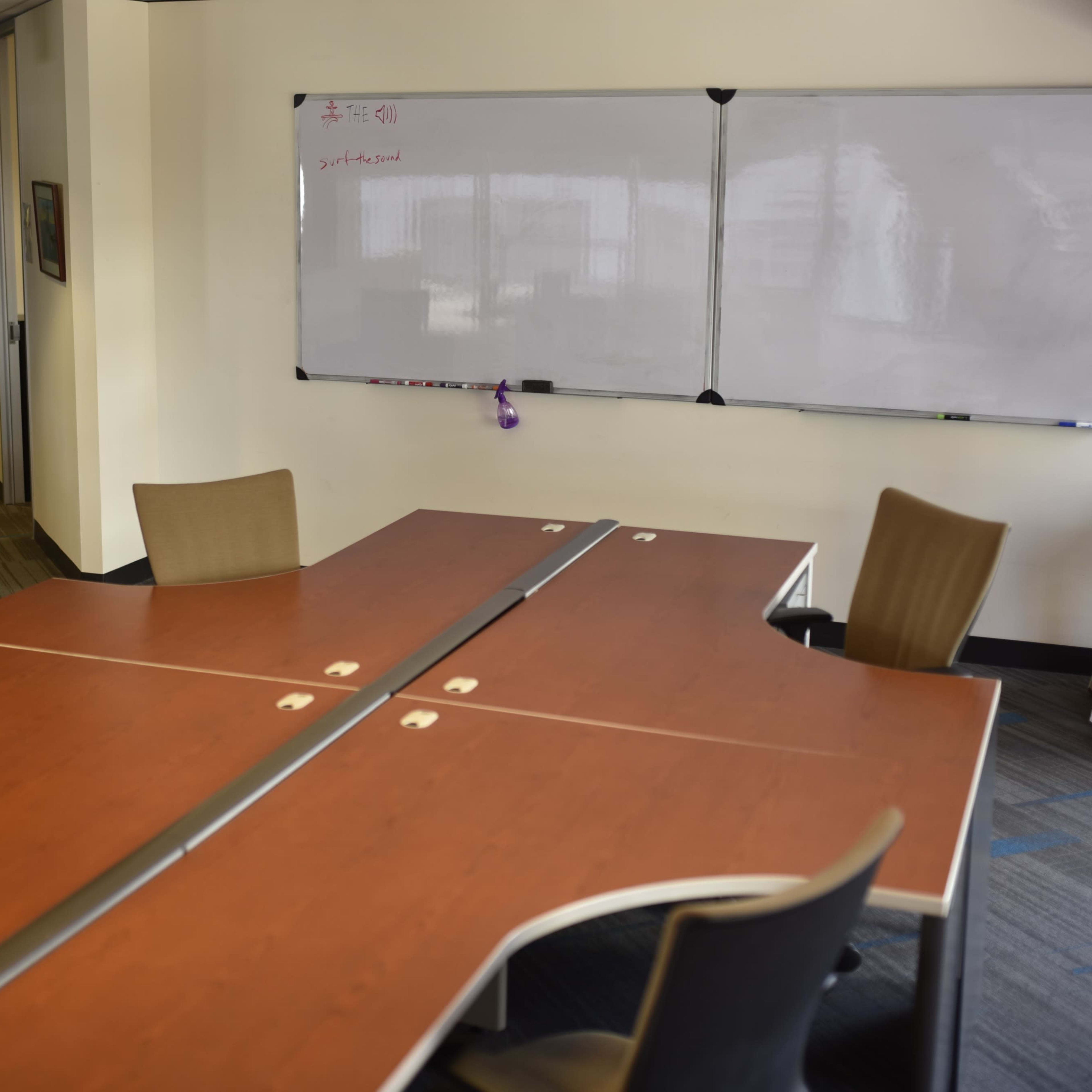 A conference room with a large wooden table and several chairs, accompanied by a whiteboard on the wall.