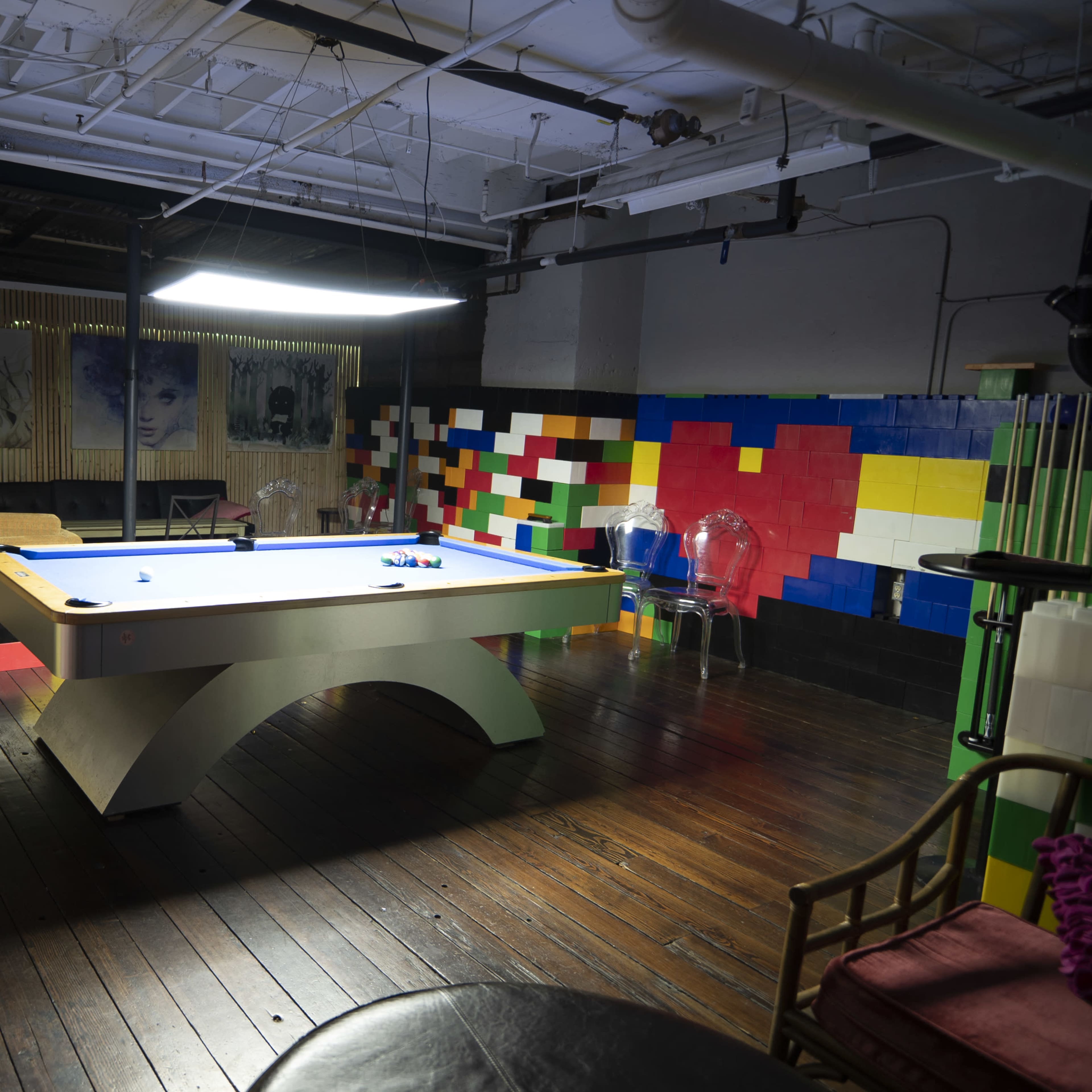 A spacious game room featuring a pool table at the center, surrounded by colorful wall decor and wooden flooring.