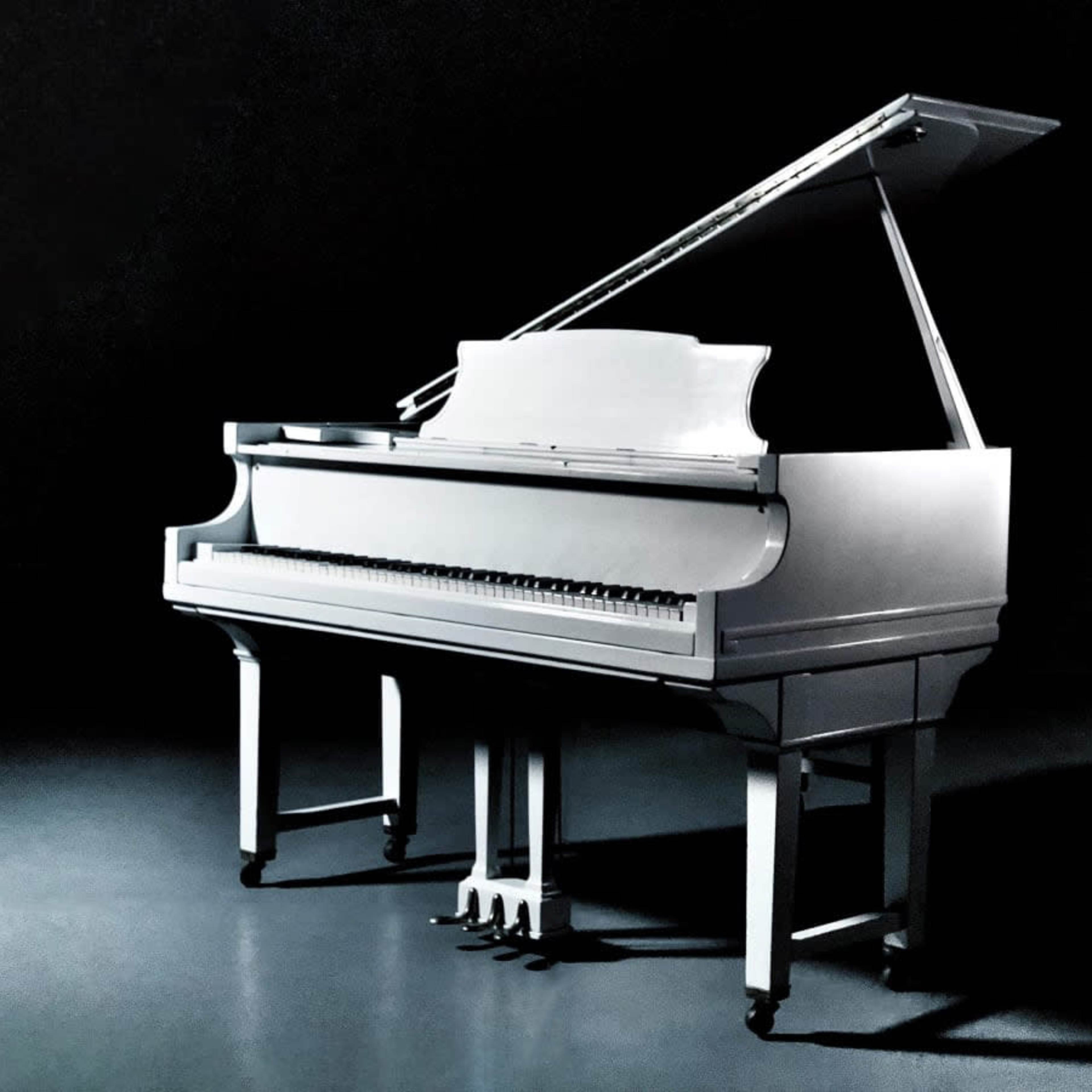 A white grand piano is positioned in a dimly lit space with its lid raised.