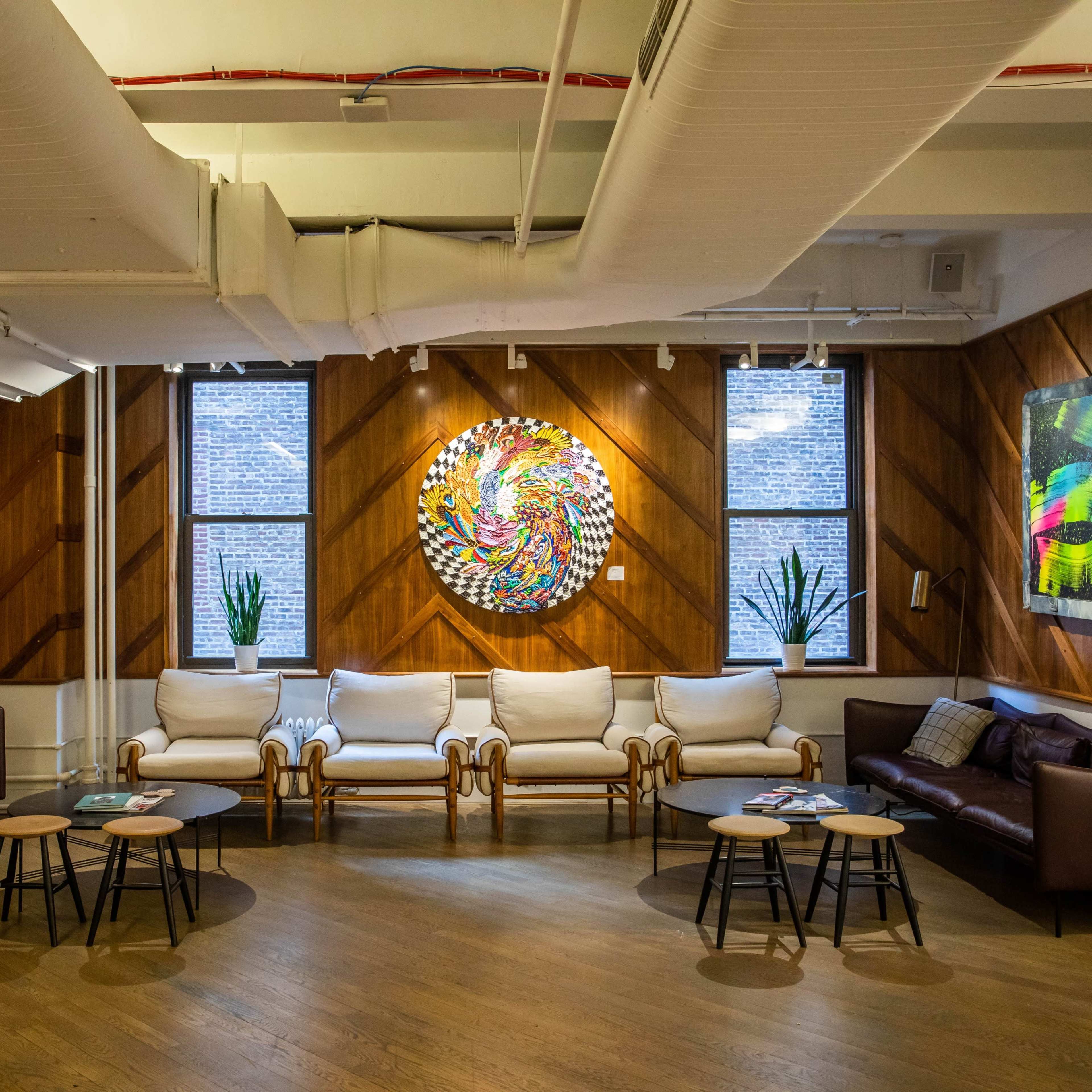 A modern lounge area with two brown sofas, a set of small round tables, and colorful abstract artwork displayed on the wooden walls.