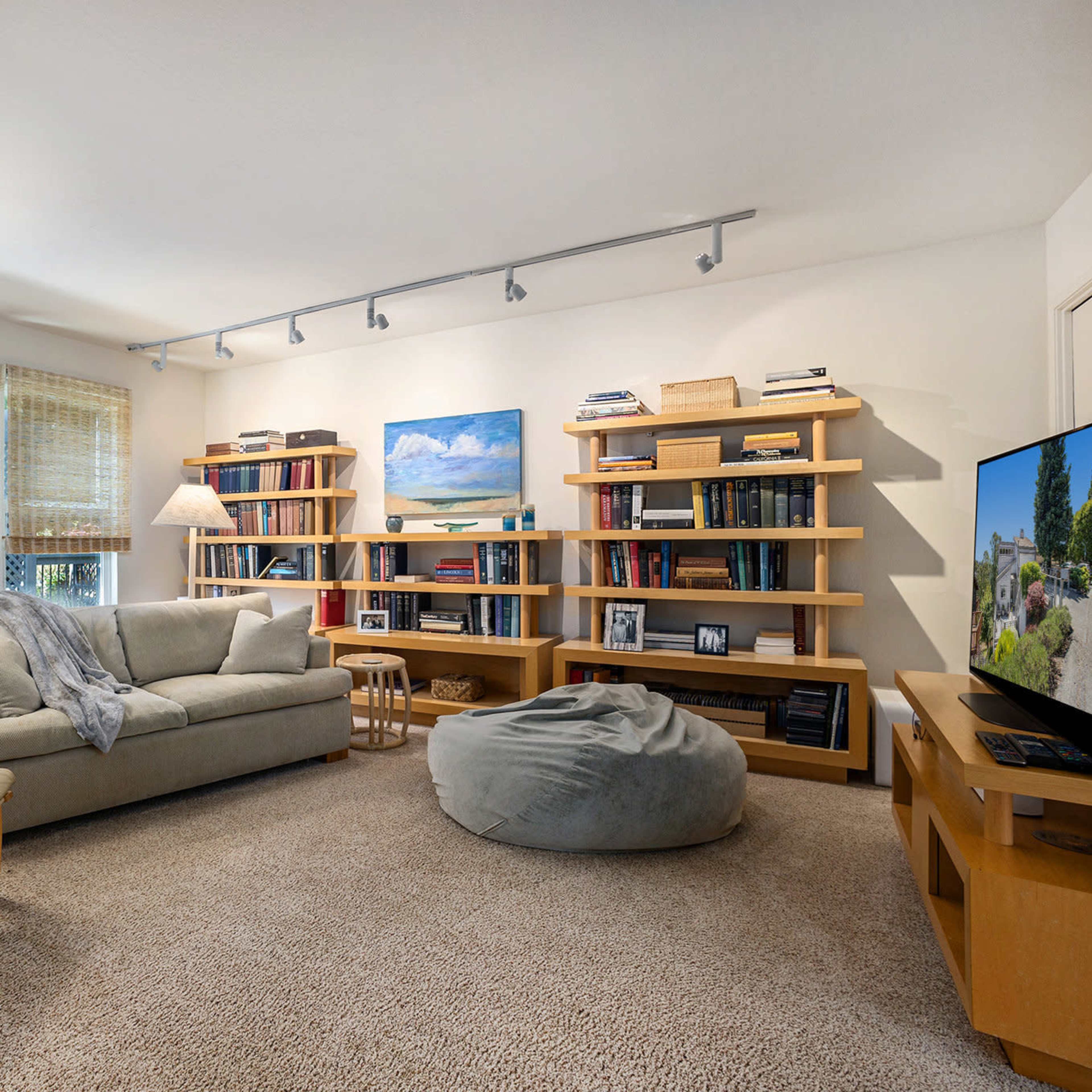 A cozy living room features a sofa, a bean bag chair, a bookshelf filled with books, and a large television against one wall.