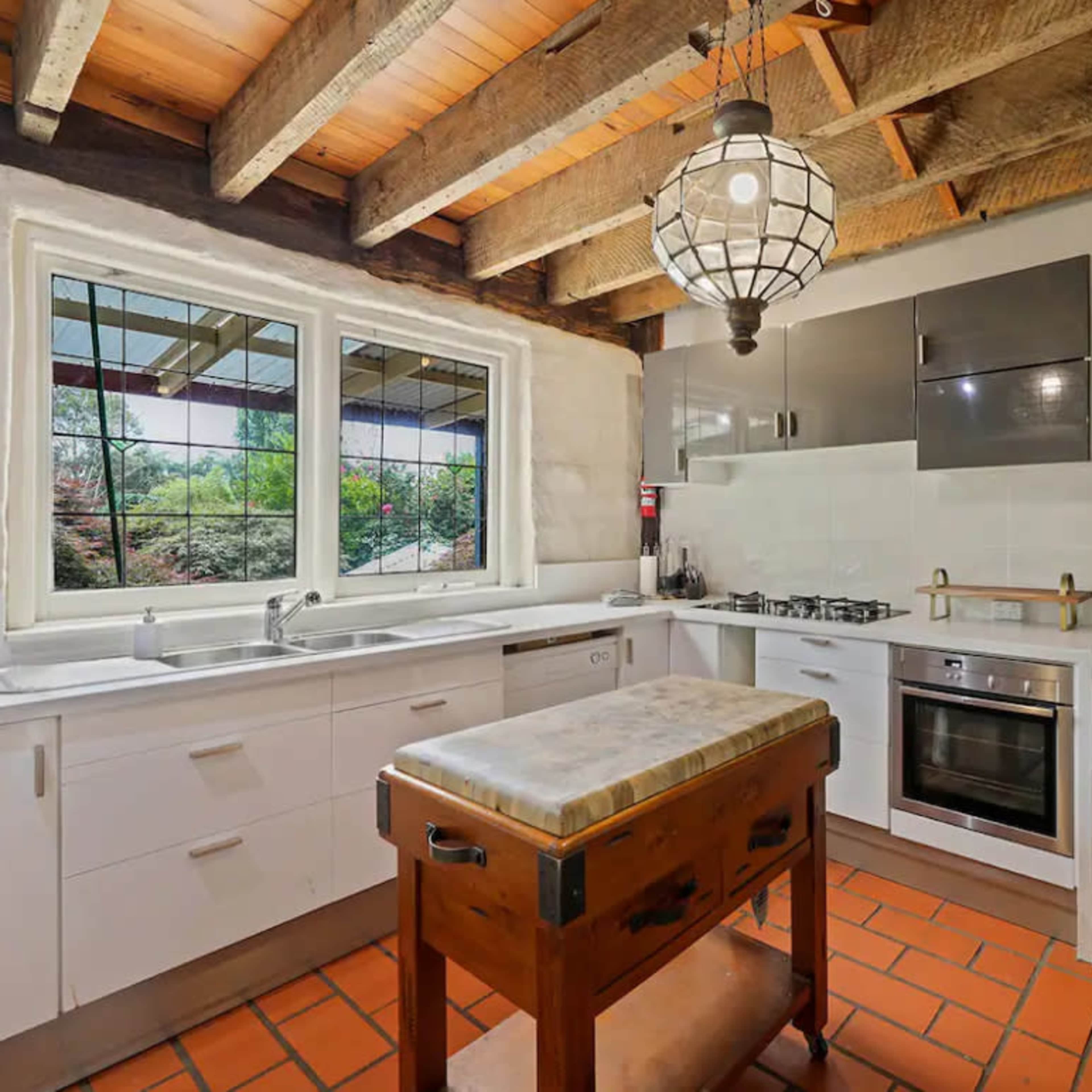 A kitchen with wooden beams, a central island, and large windows overlooking a garden.