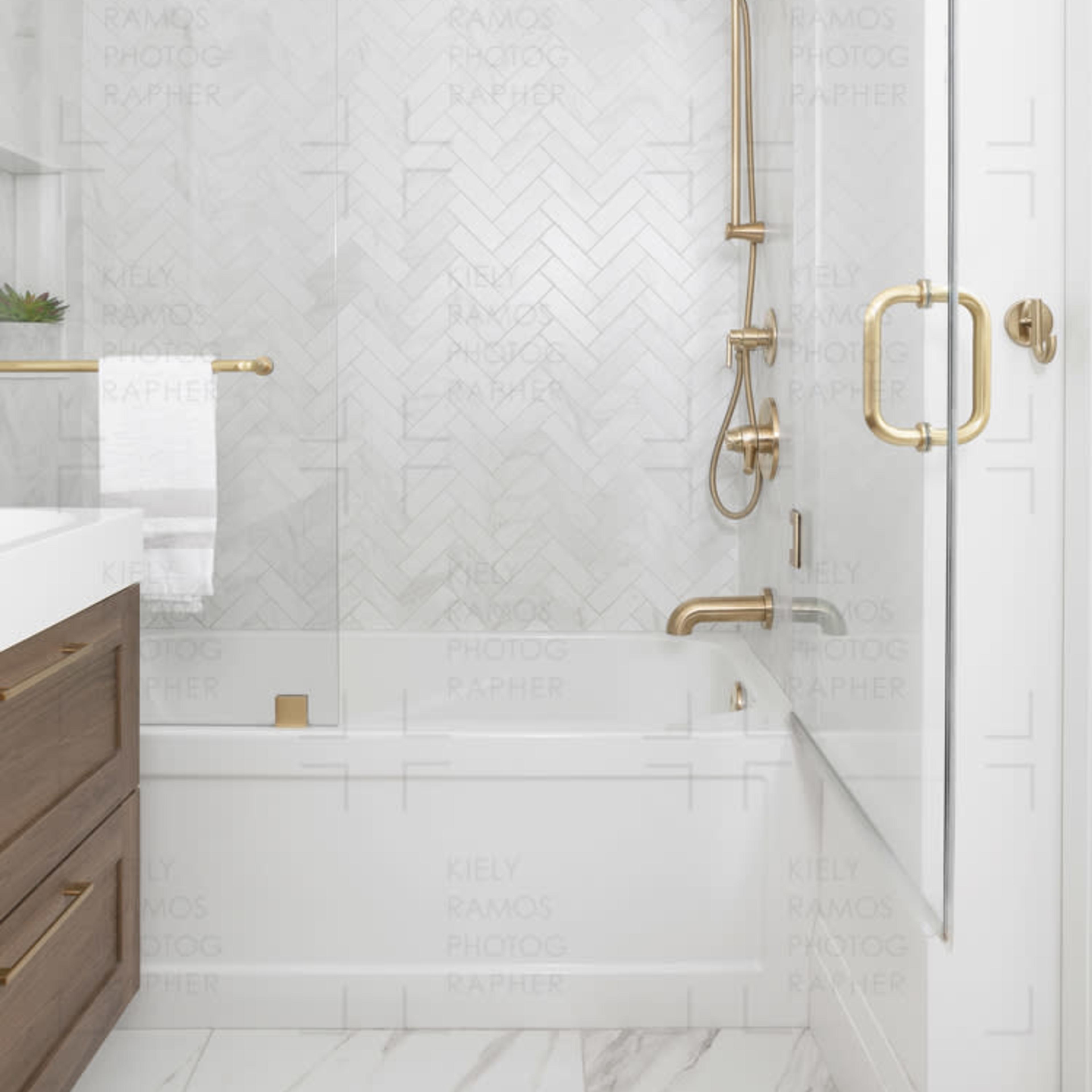 A modern bathroom featuring a glass shower enclosure, herringbone tile pattern, and gold fixtures.