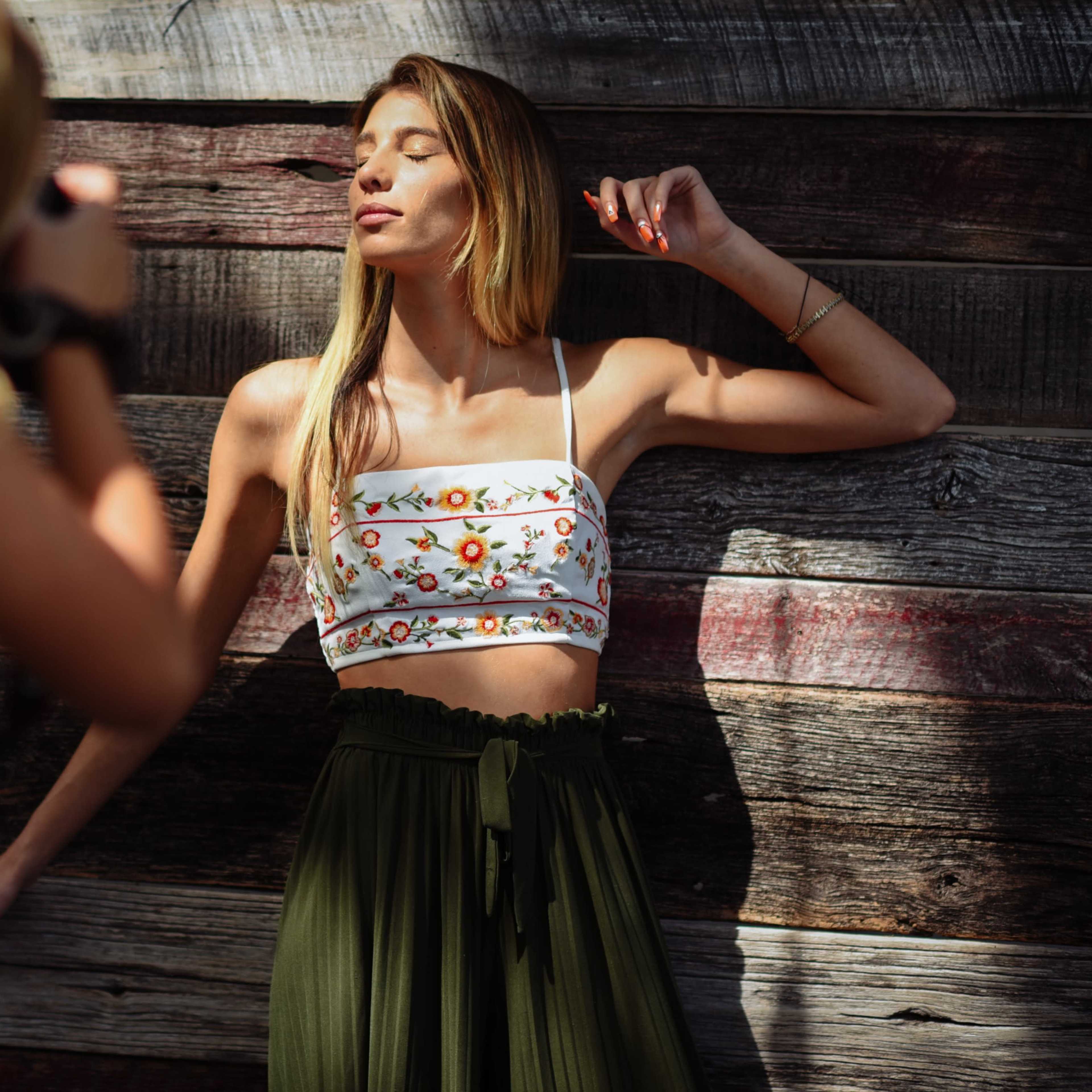 A woman poses against a wooden wall while another woman takes her picture.