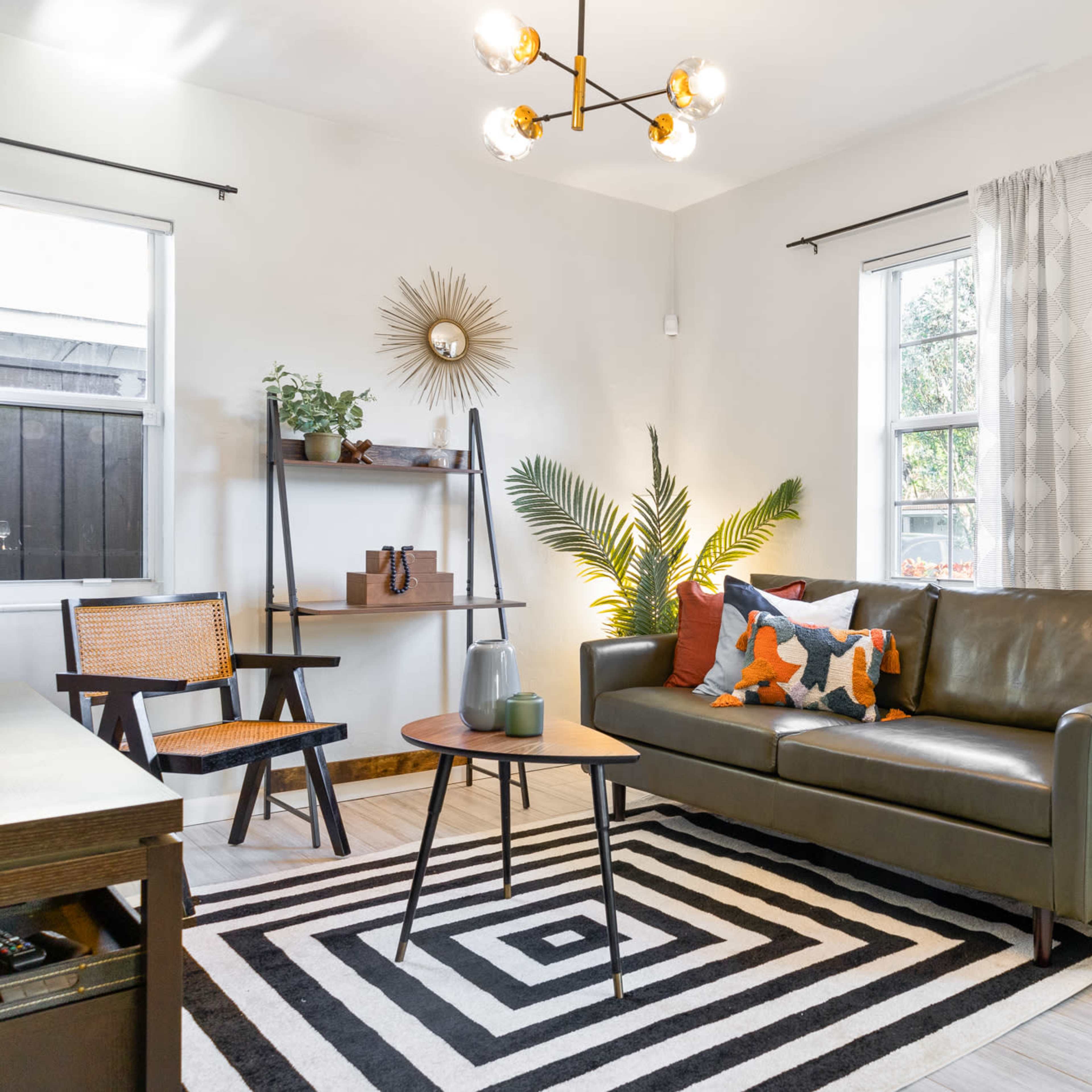 A modern living room features a leather sofa, geometric art on the walls, and a striped area rug under a coffee table.