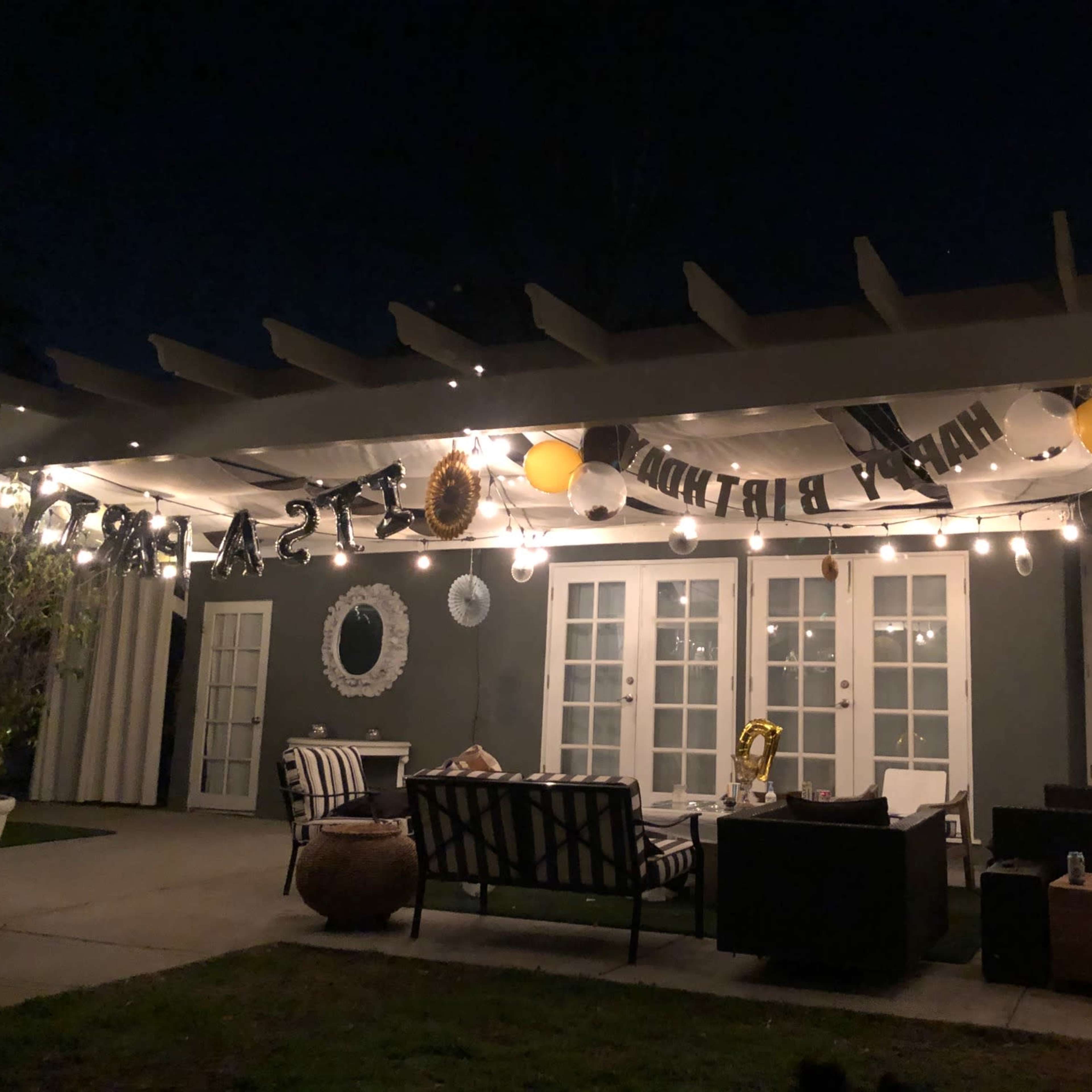 A patio is decorated with string lights and balloons for a birthday celebration at night.
