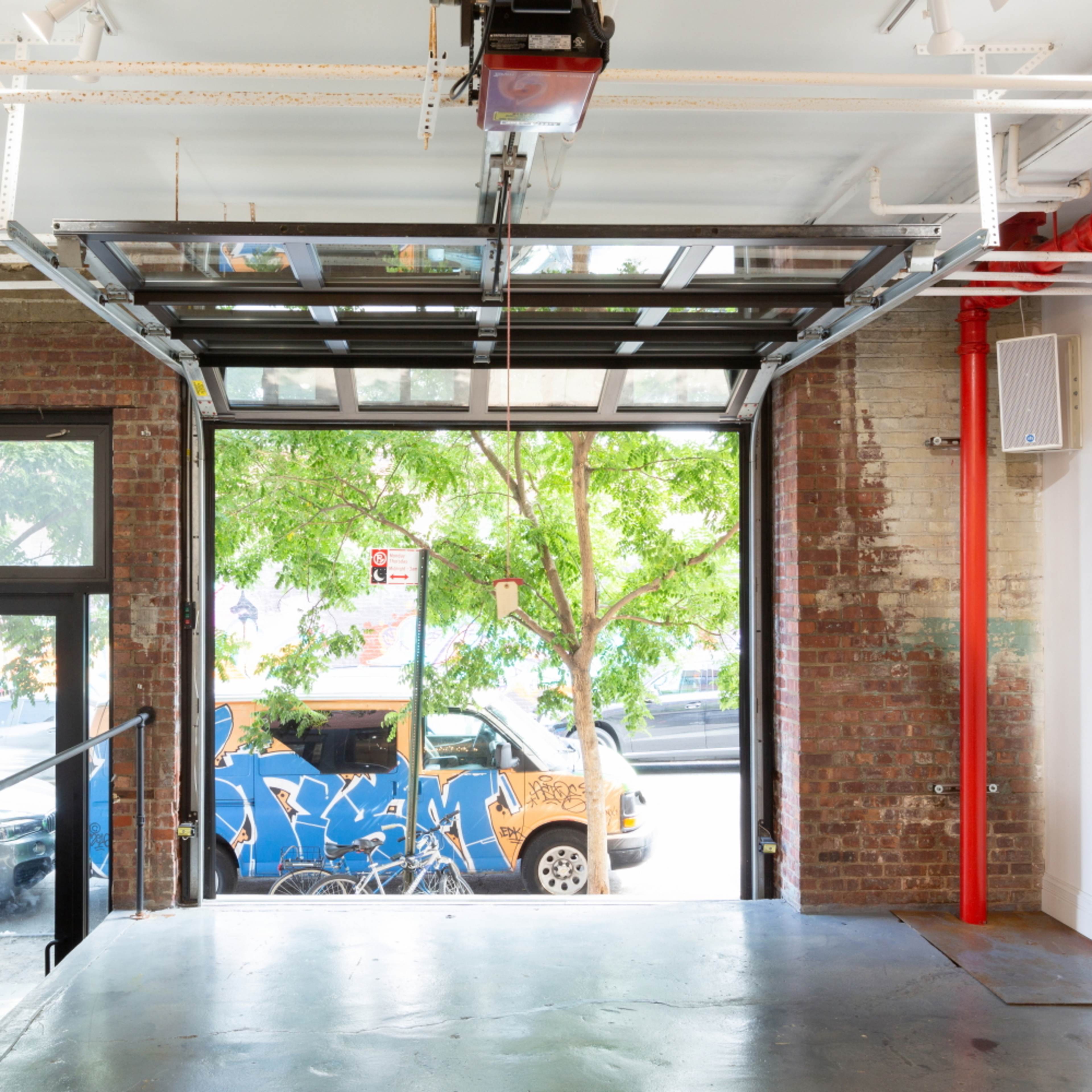 A garage space with a large glass door open to a street view, featuring a brick wall and a painted van outside.