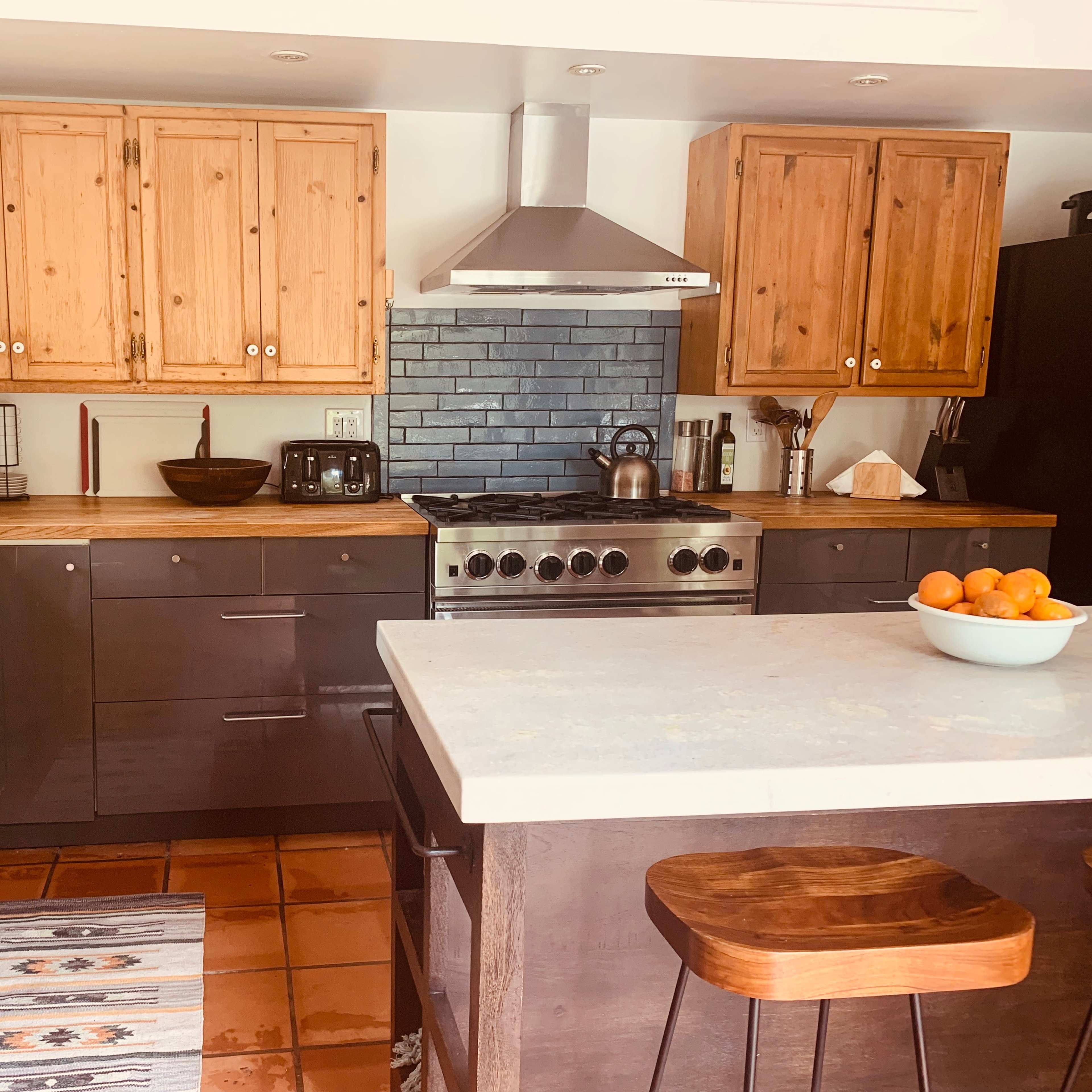 A modern kitchen with wooden cabinetry, stainless steel appliances, and a central island topped with a bowl of oranges.