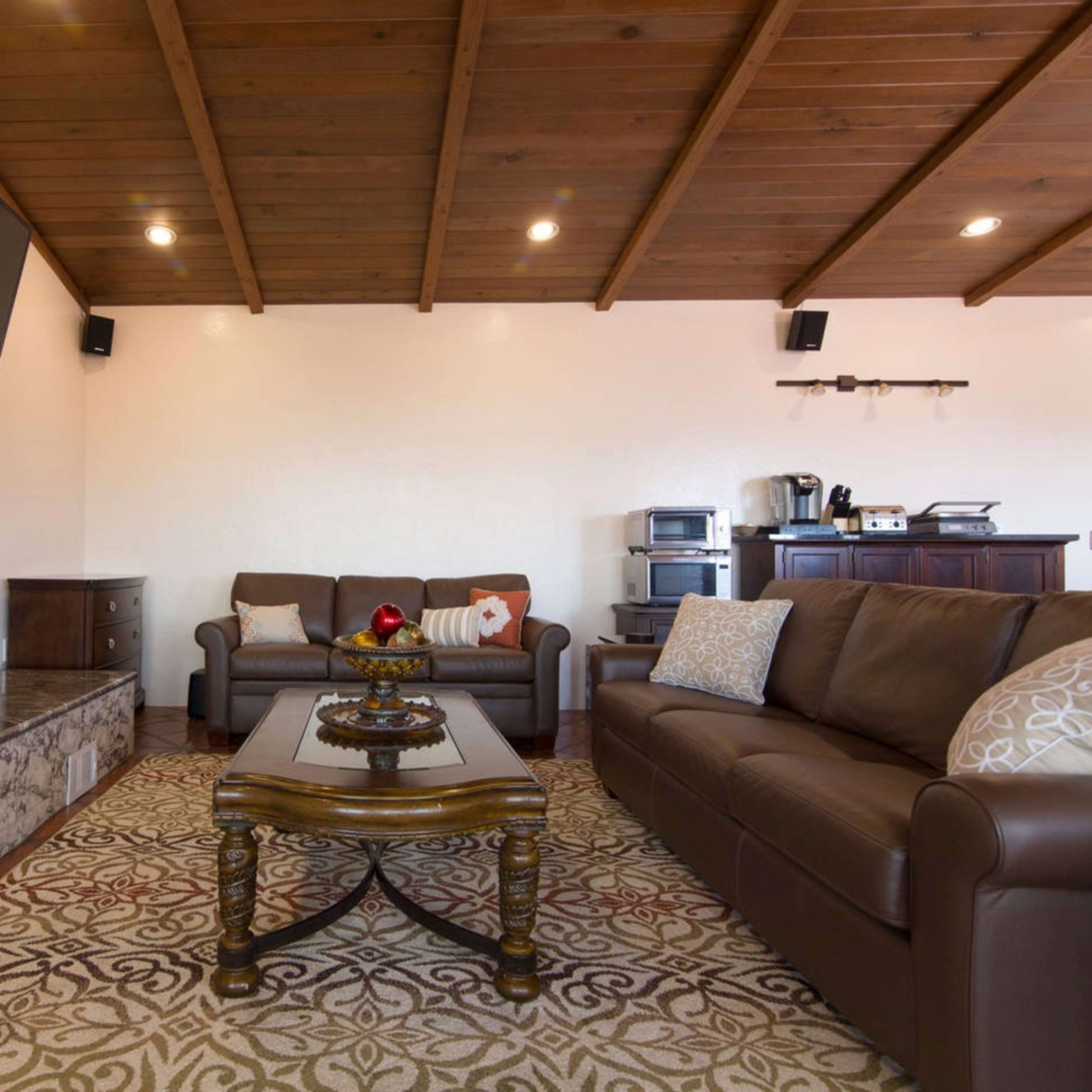 A living room featuring a large television mounted on a wooden ceiling, a marble fireplace, and two sofas facing a coffee table.