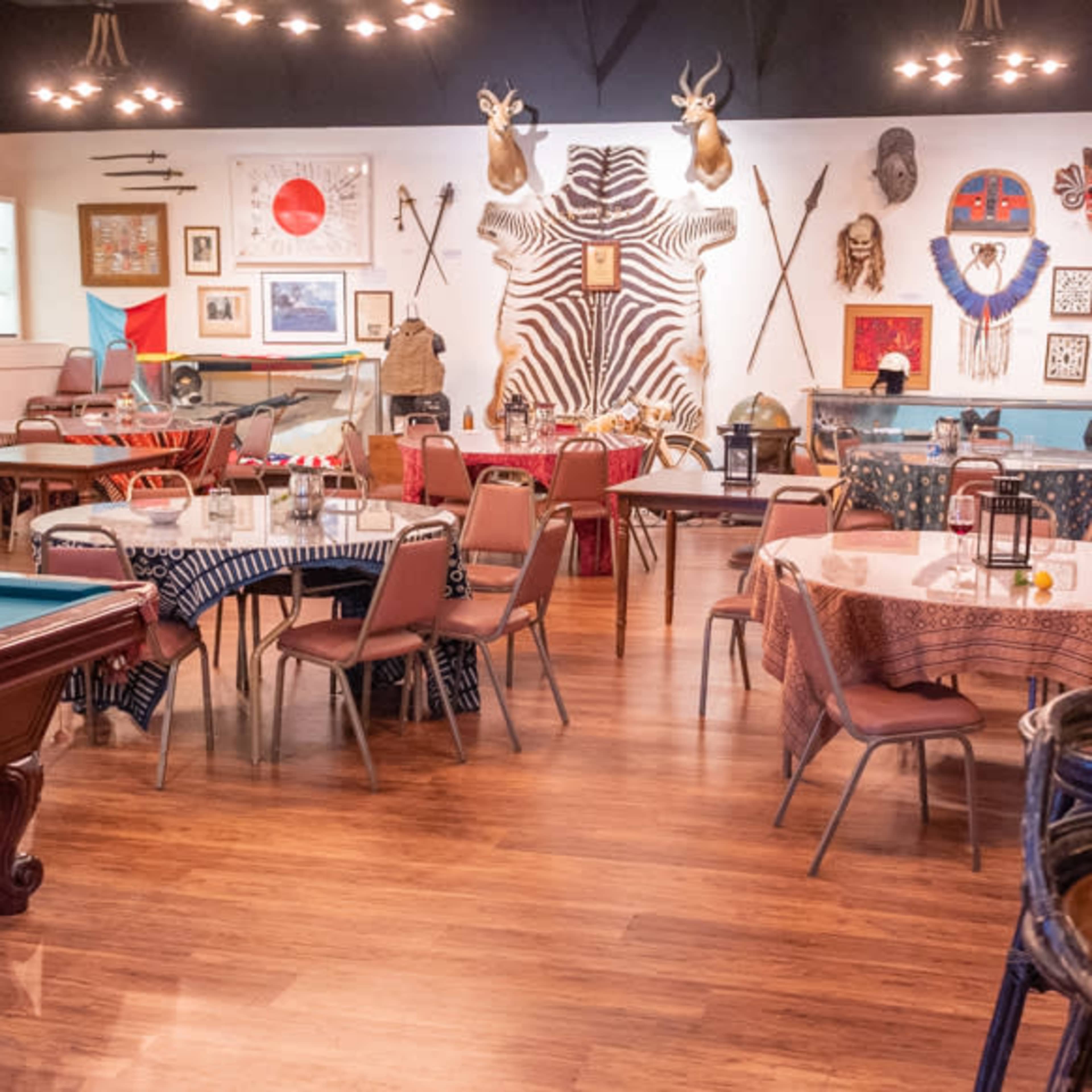 A restaurant interior featuring several tables, a pool table, and walls adorned with animal mounts and various artifacts.