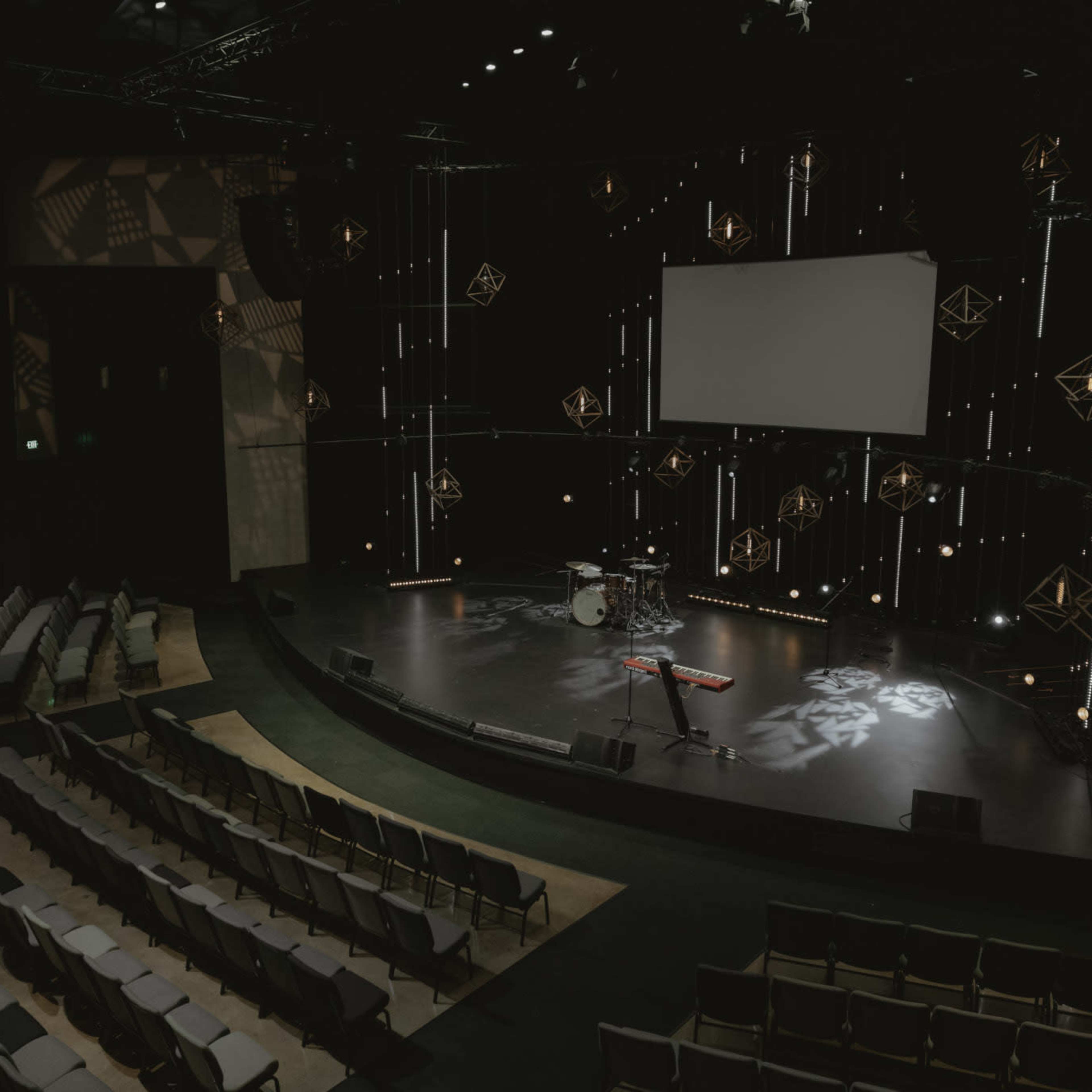 An empty auditorium stage with a drum set and keyboard, surrounded by rows of seats.