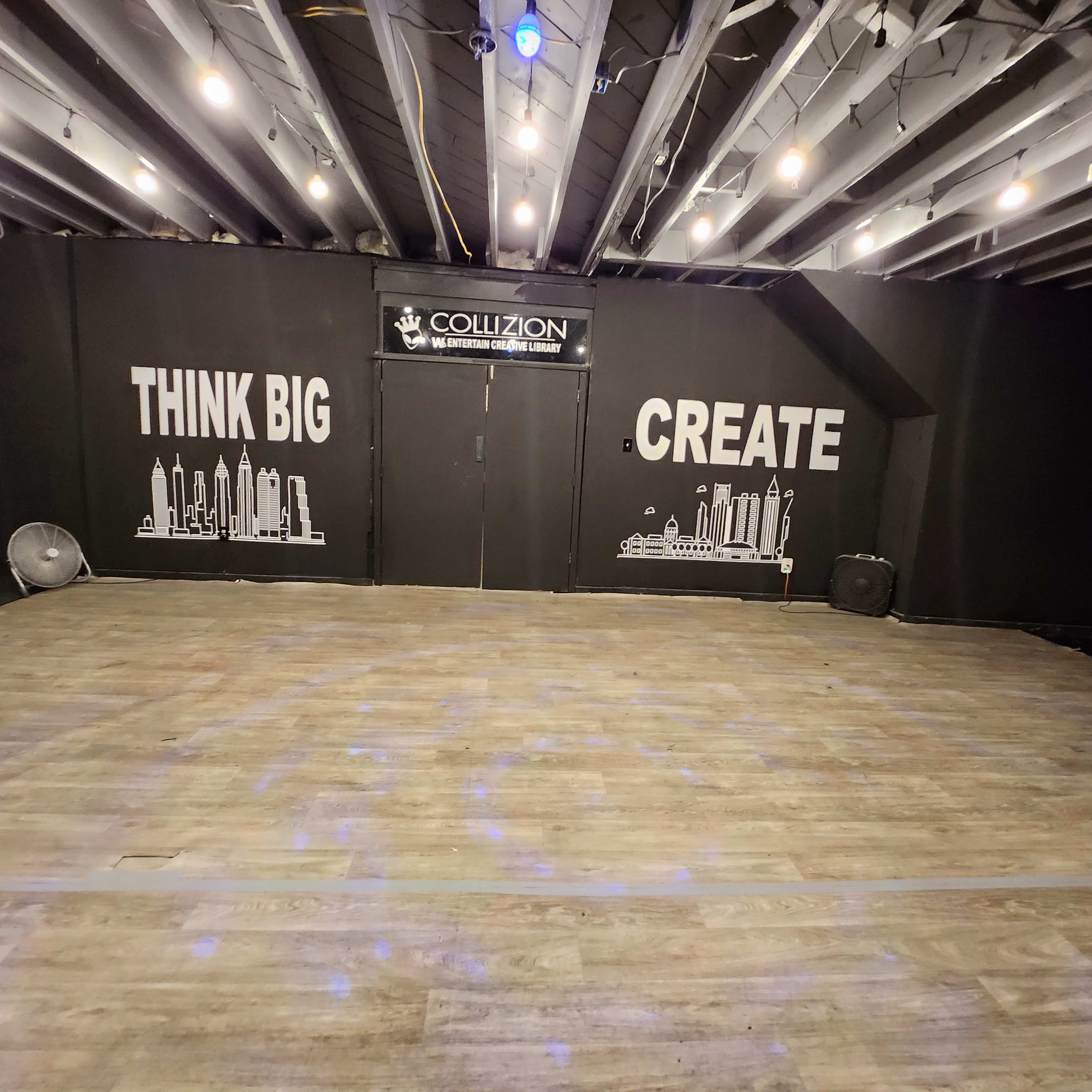A dimly lit room with a wooden floor and black walls featuring the phrases "THINK BIG" and "CREATE," along with some city skyline graphics.