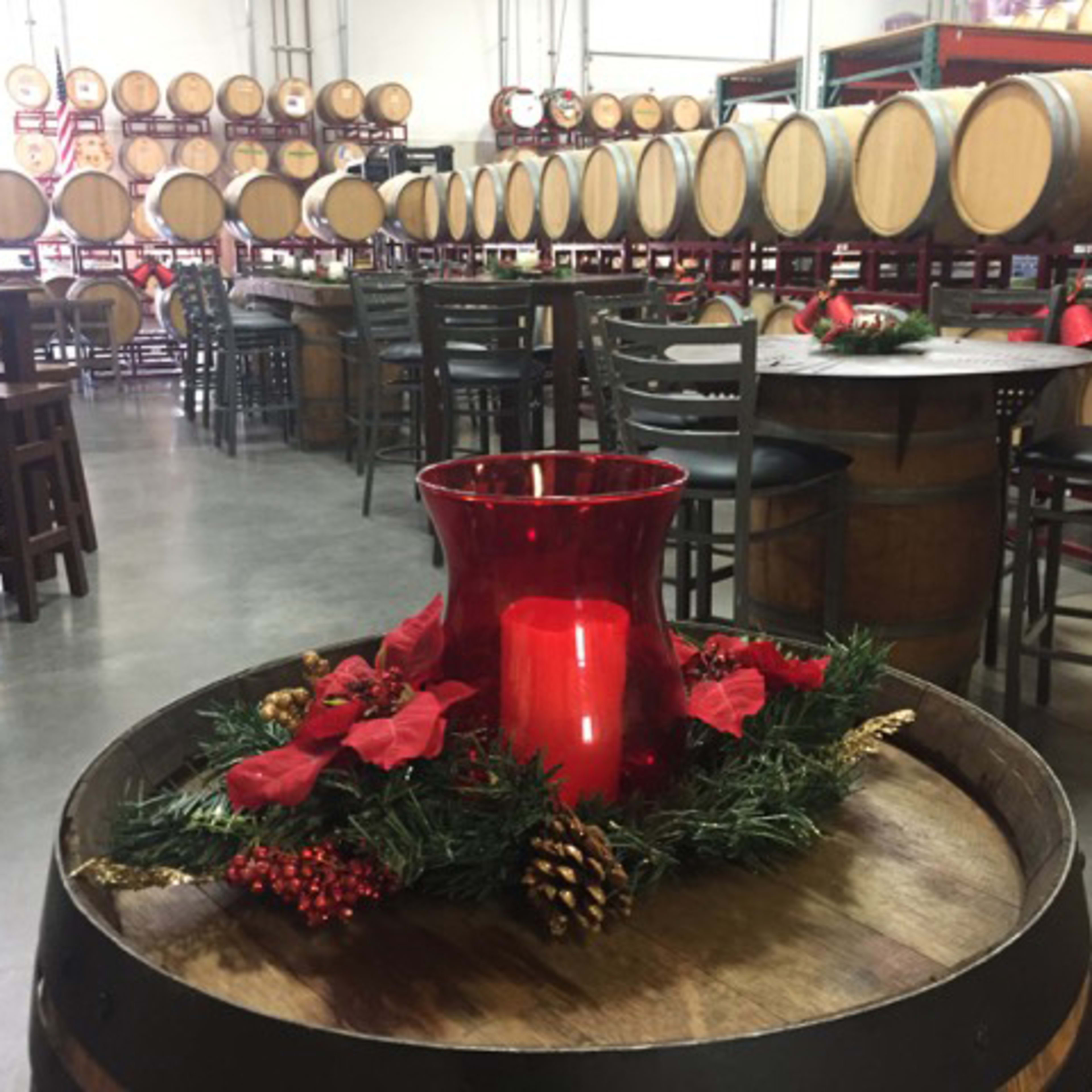 A winery interior with wooden barrels, tables, and festive holiday decorations including a red candle surrounded by greenery.