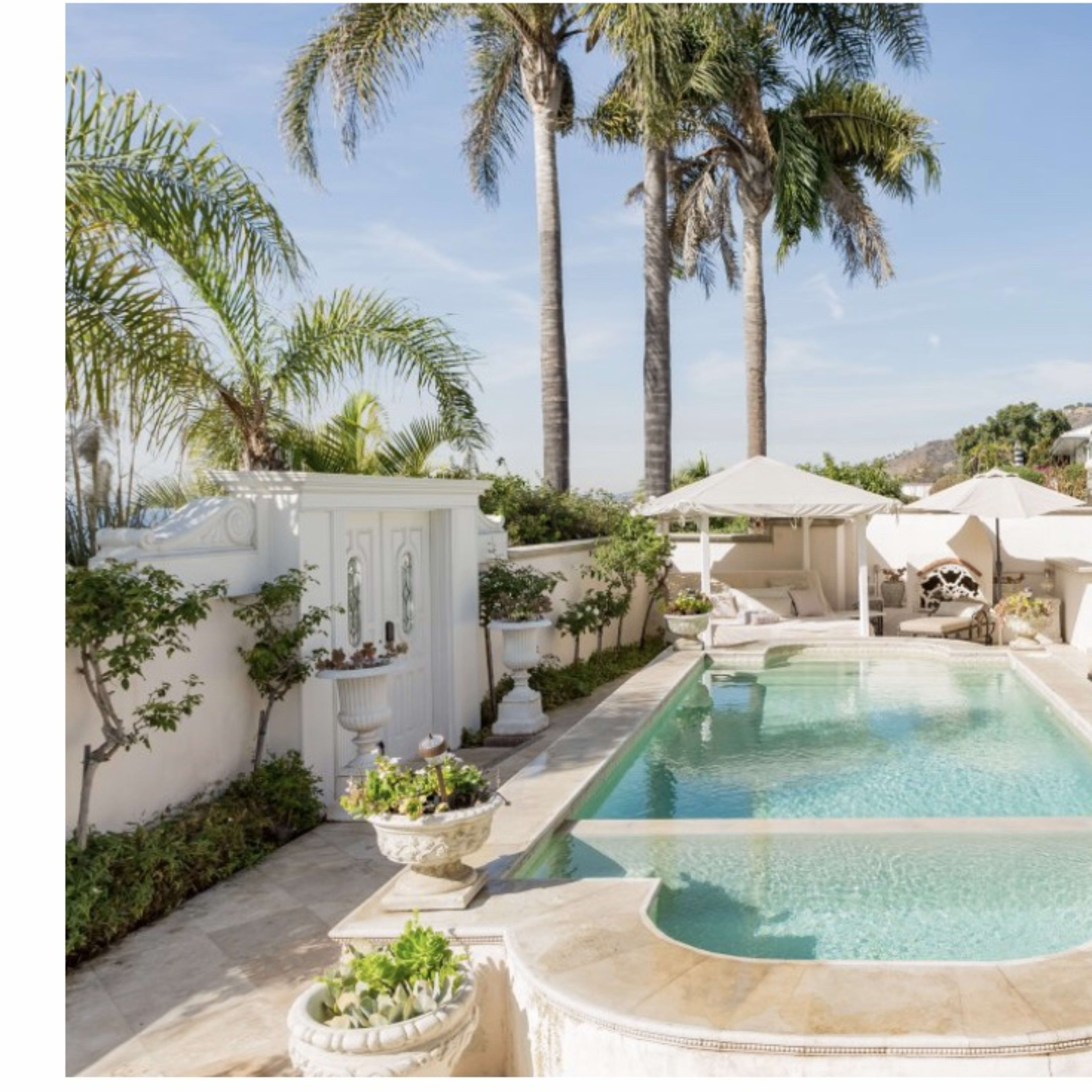 A landscaped pool area surrounded by white loungers, palm trees, and a terrace with decorative planters.