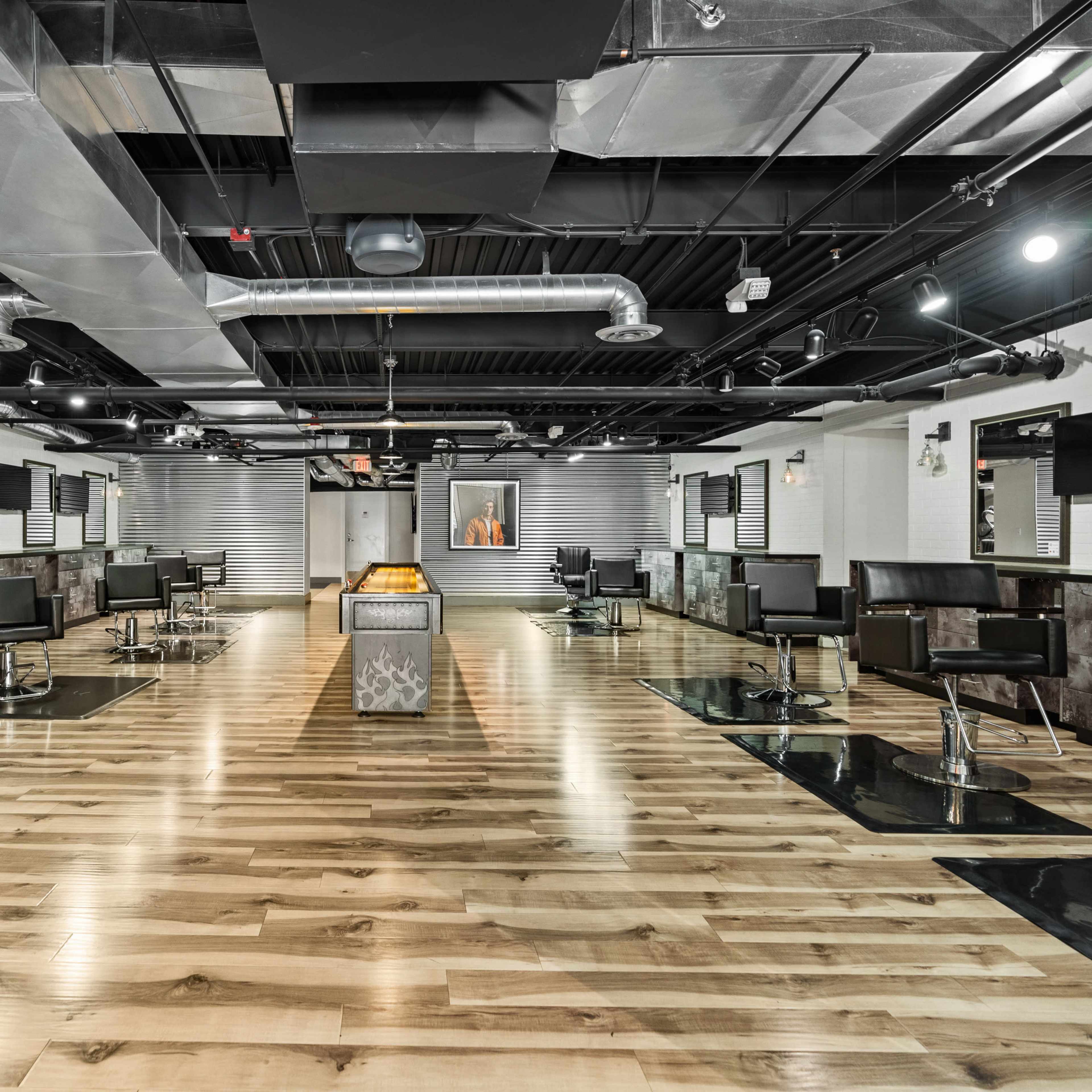 A modern barbershop interior with multiple styling stations, black chairs, and polished wooden flooring under bright overhead lighting.