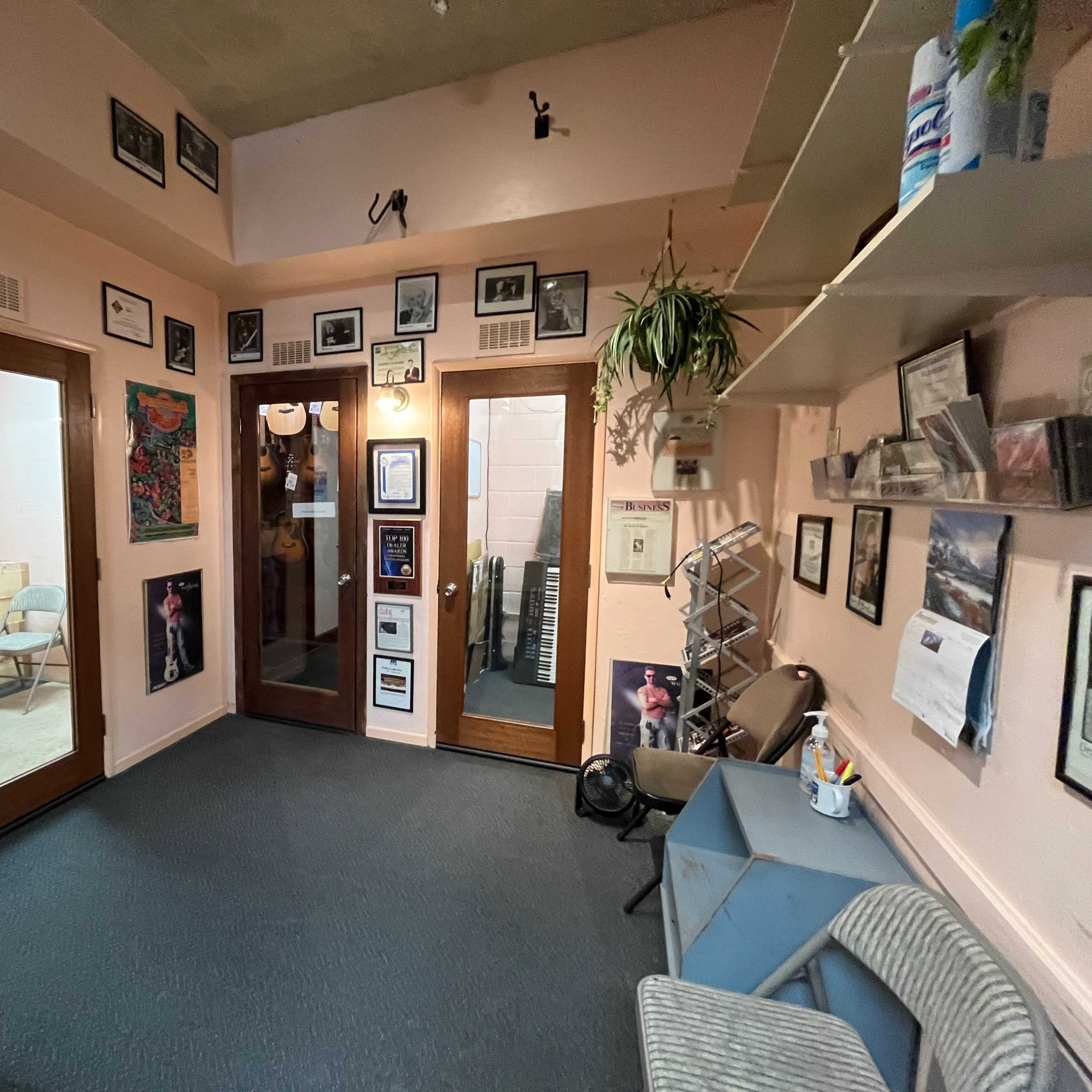 A small, neatly organized room with multiple doors, framed photos on the walls, and a few chairs and shelves.