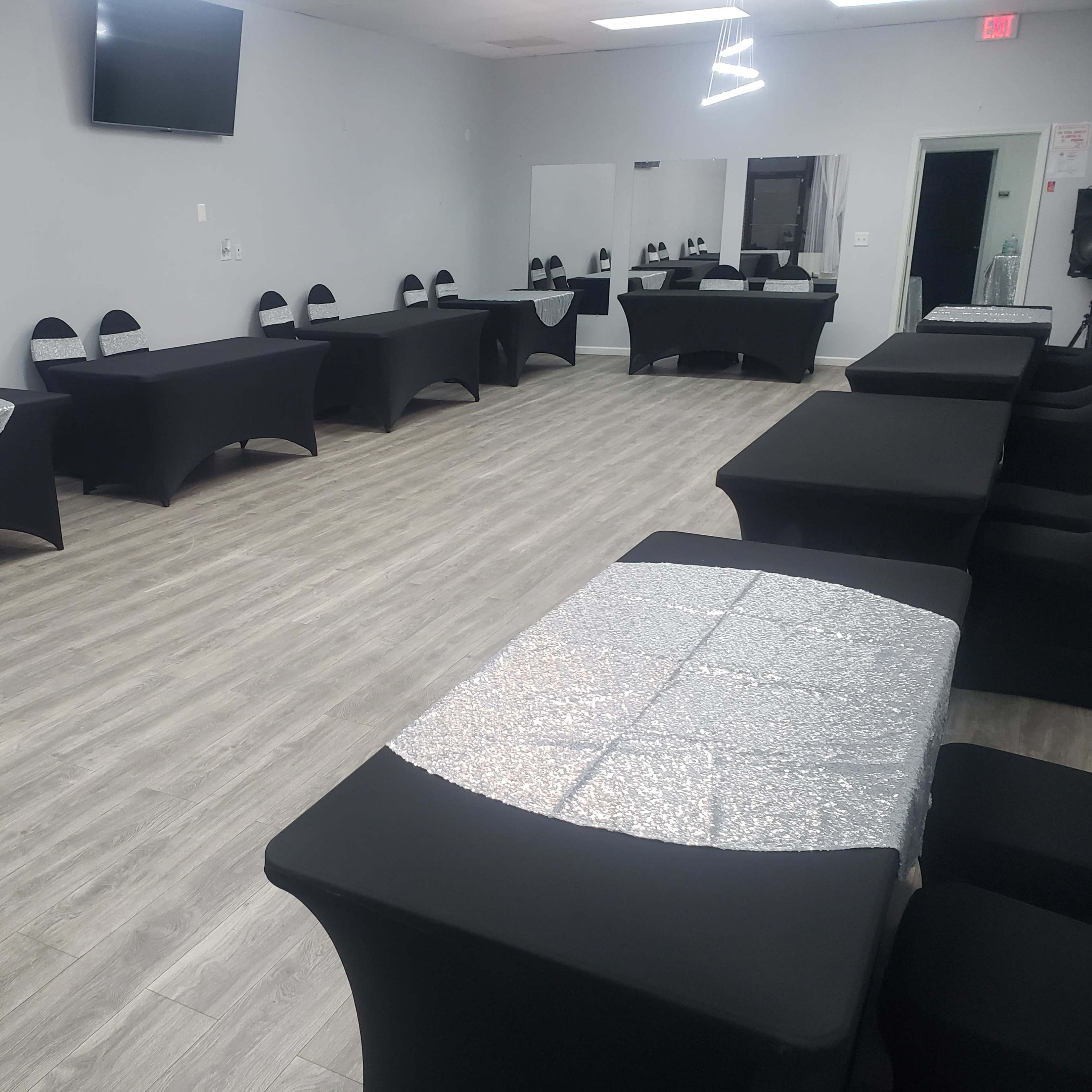 A spacious event room featuring several tables covered with black and silver tablecloths arranged in a neat layout.
