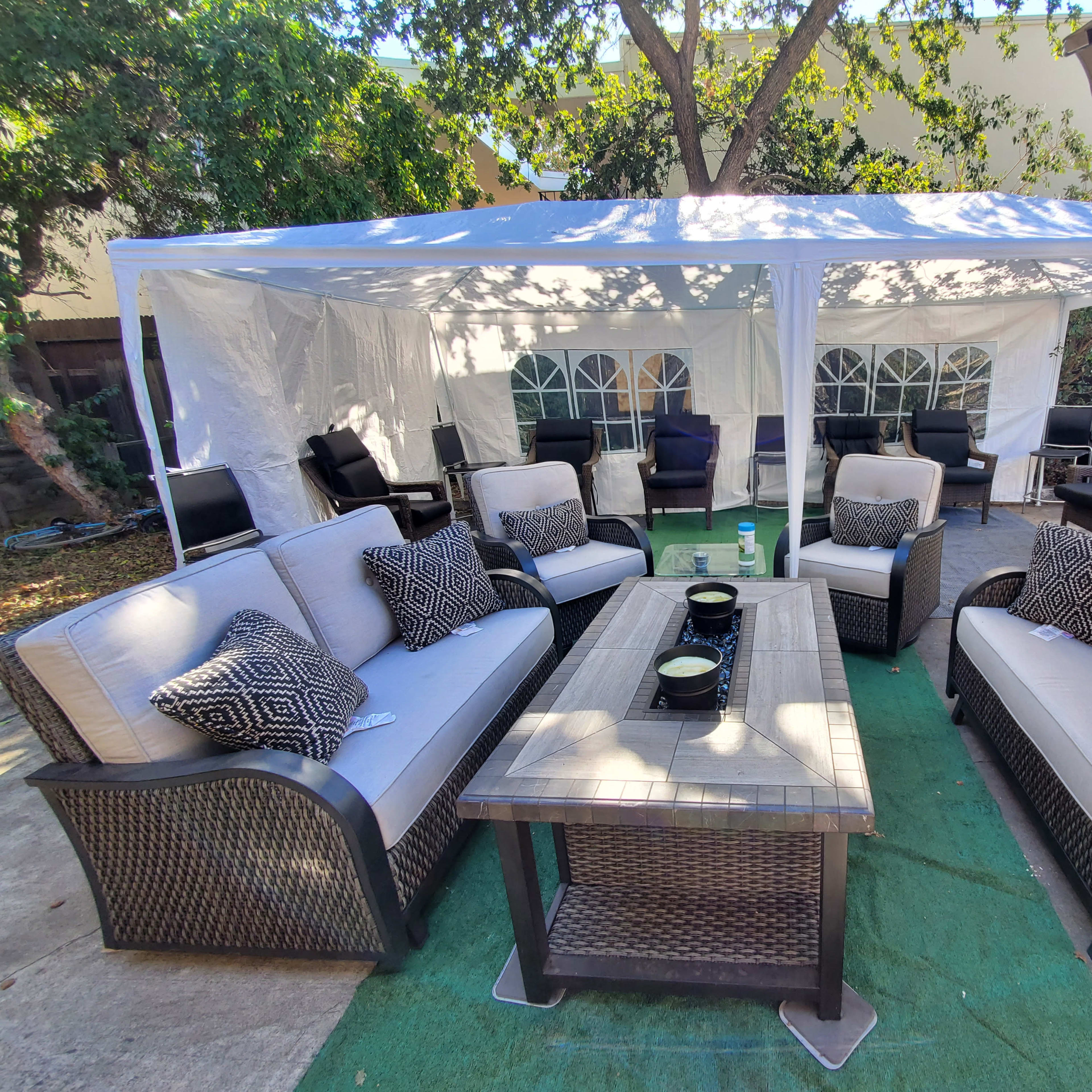 A spacious outdoor seating area features two sets of sofas and a coffee table under a white tent surrounded by chairs.