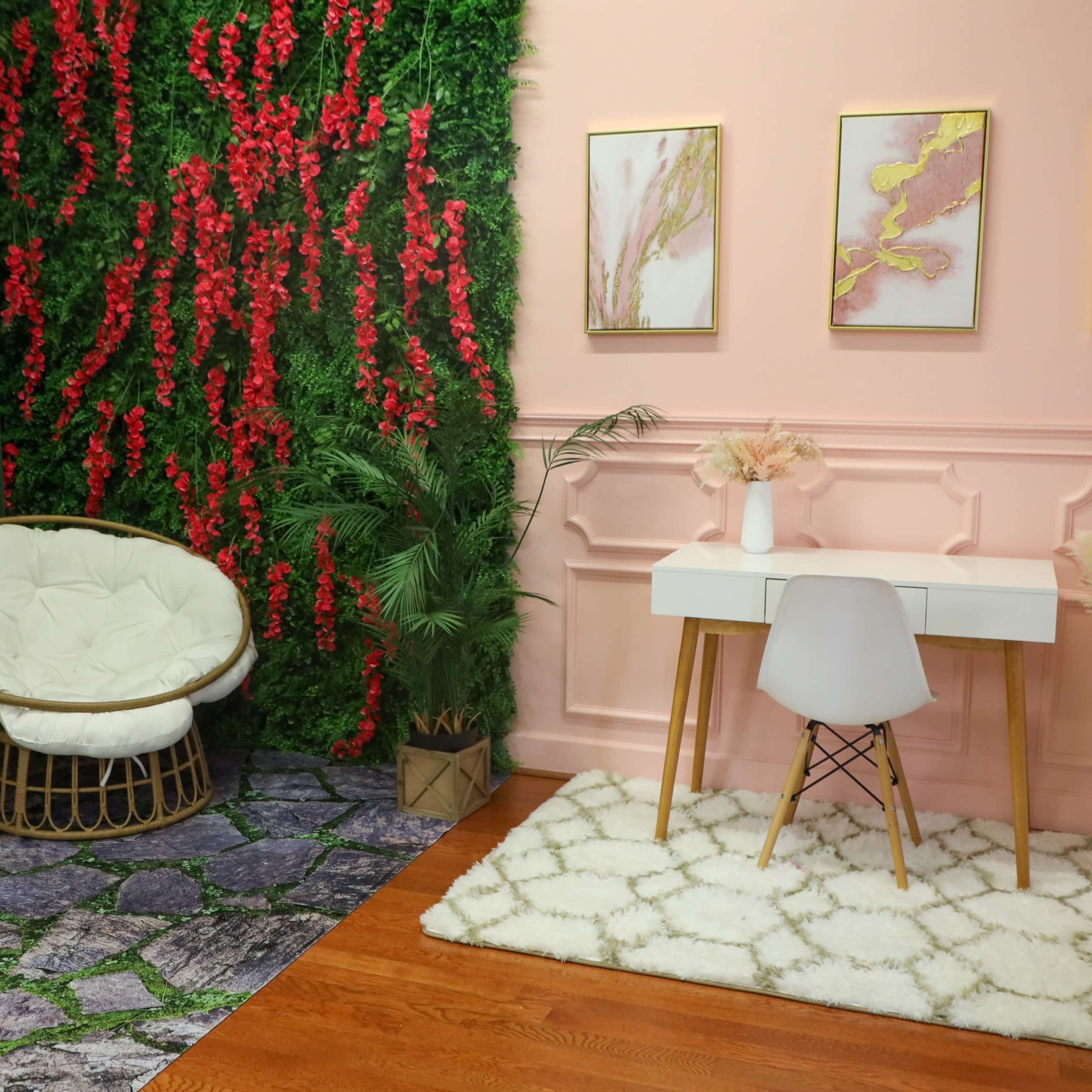 A stylish indoor space with a green wall featuring red foliage, a white cushioned chair, a minimalist desk, and decorative art on the pink wall.