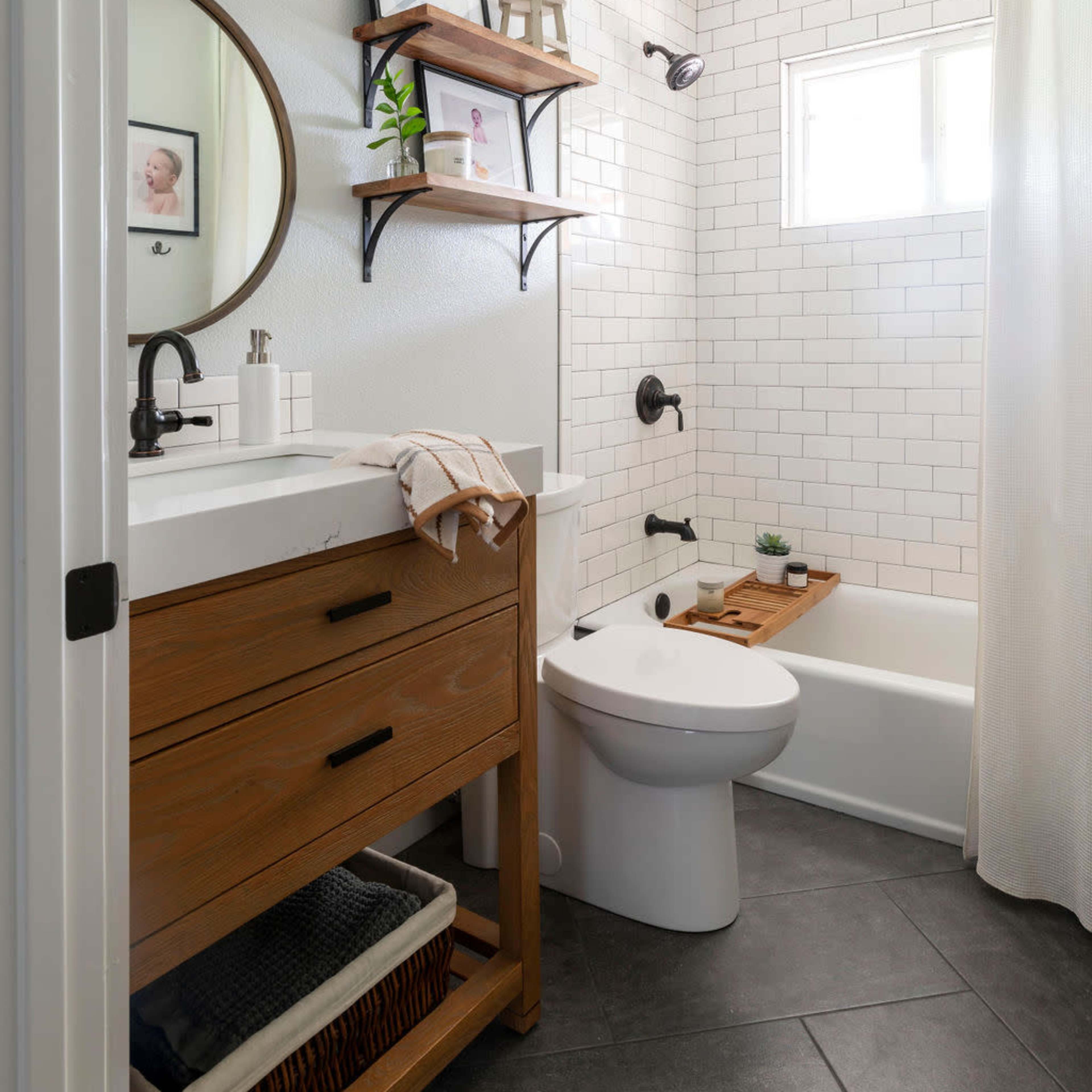 A modern bathroom features a tub with a shower, a wall-mounted mirror, wooden shelves, and a vanity with a sink.