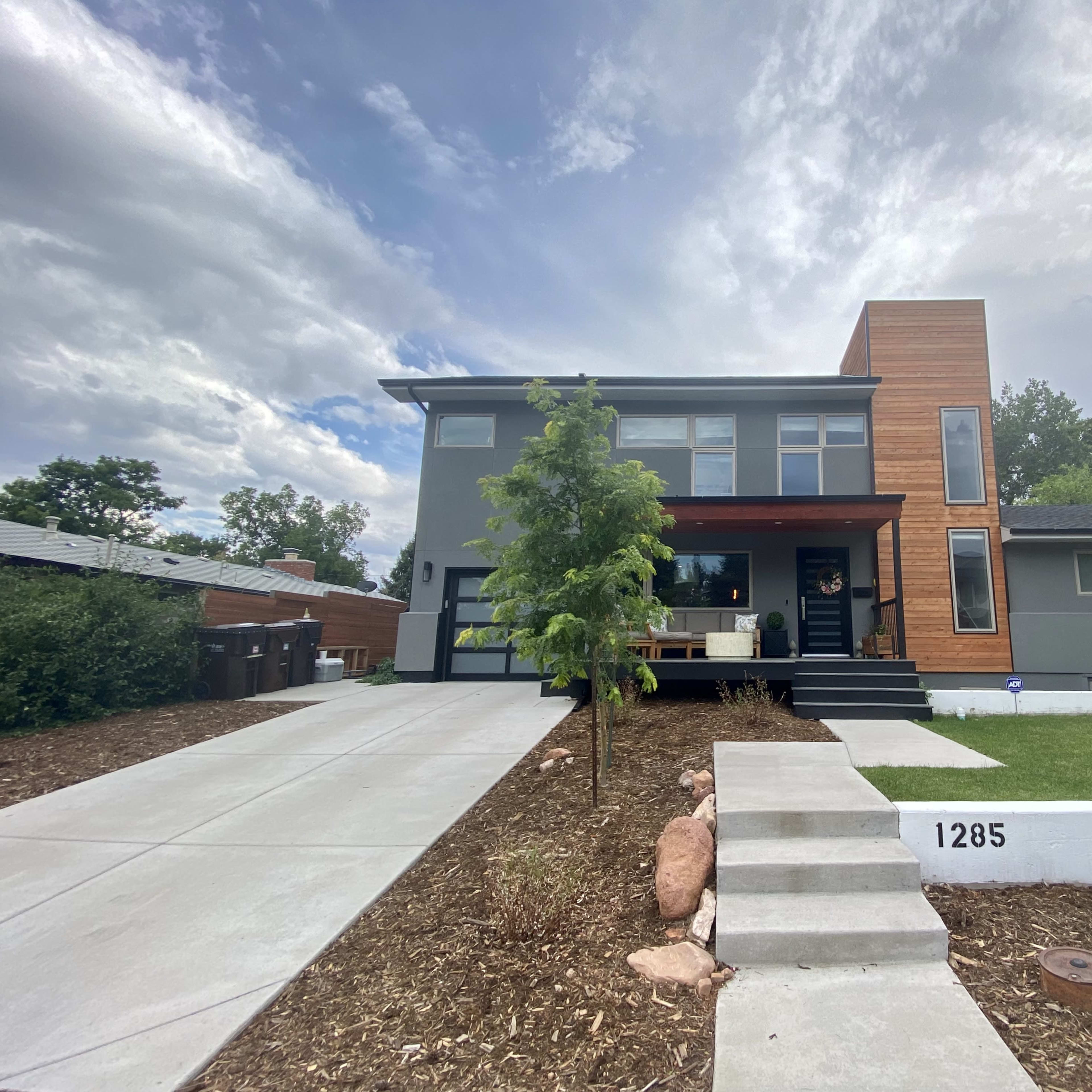 A modern two-story house with a mix of gray and wooden siding, featuring a landscaped front yard and a concrete driveway.