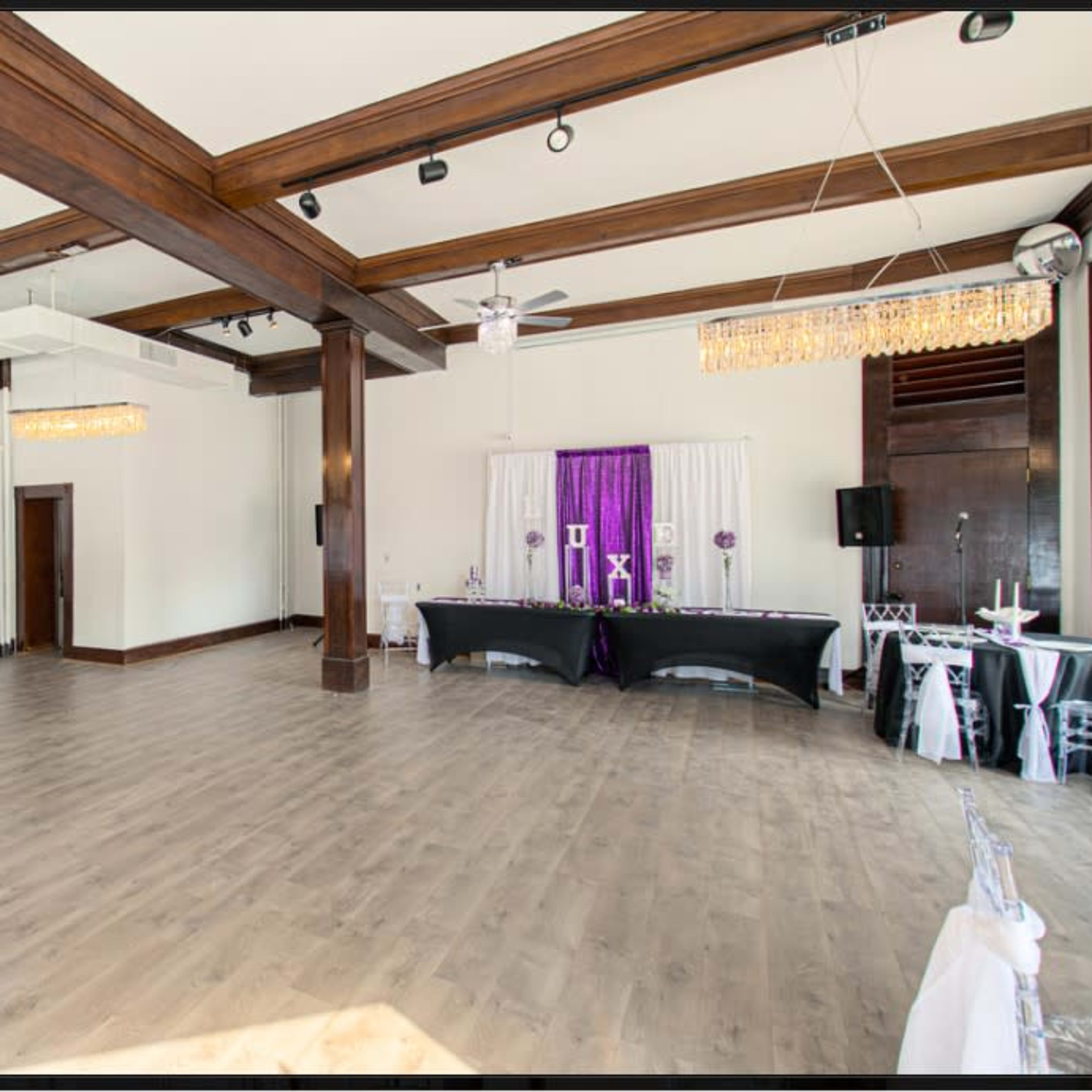 A spacious event hall featuring wooden beams, modern lighting, and tables set up along the sides.