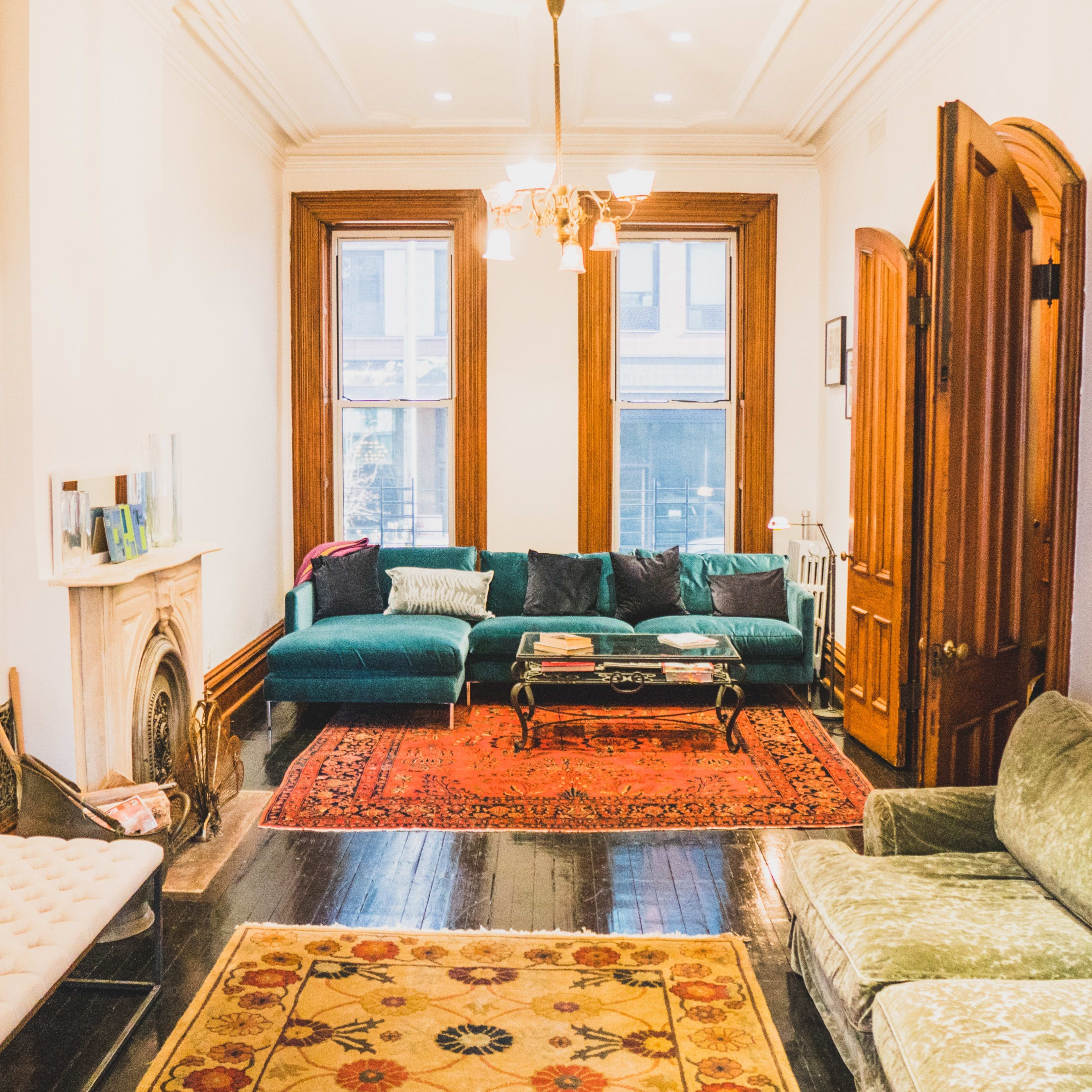 A bright living room with a mix of green sofas, ornate rugs, and framed photographs on the walls.
