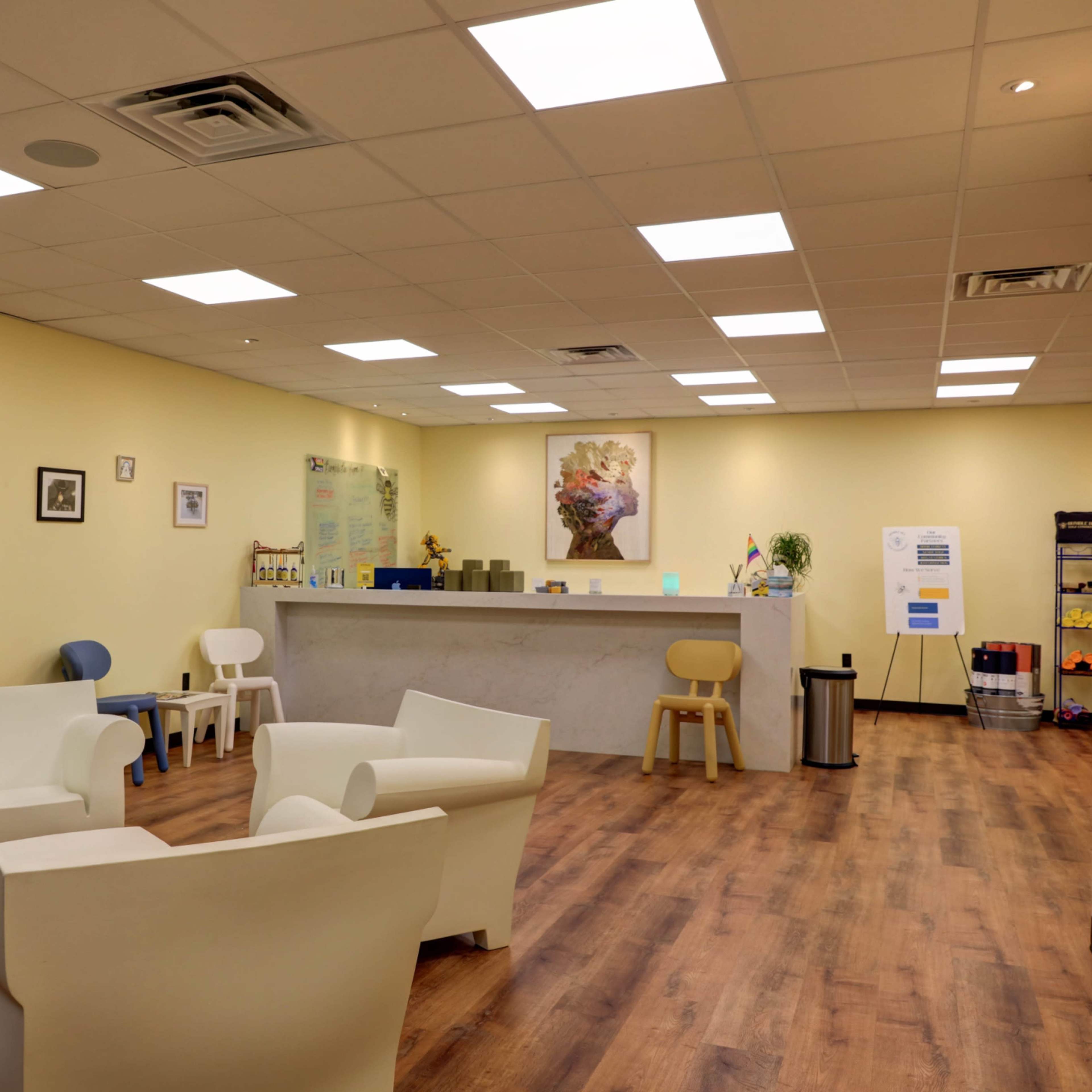 A bright, modern waiting area with light yellow walls, a reception counter, and several white chairs arranged around the space.