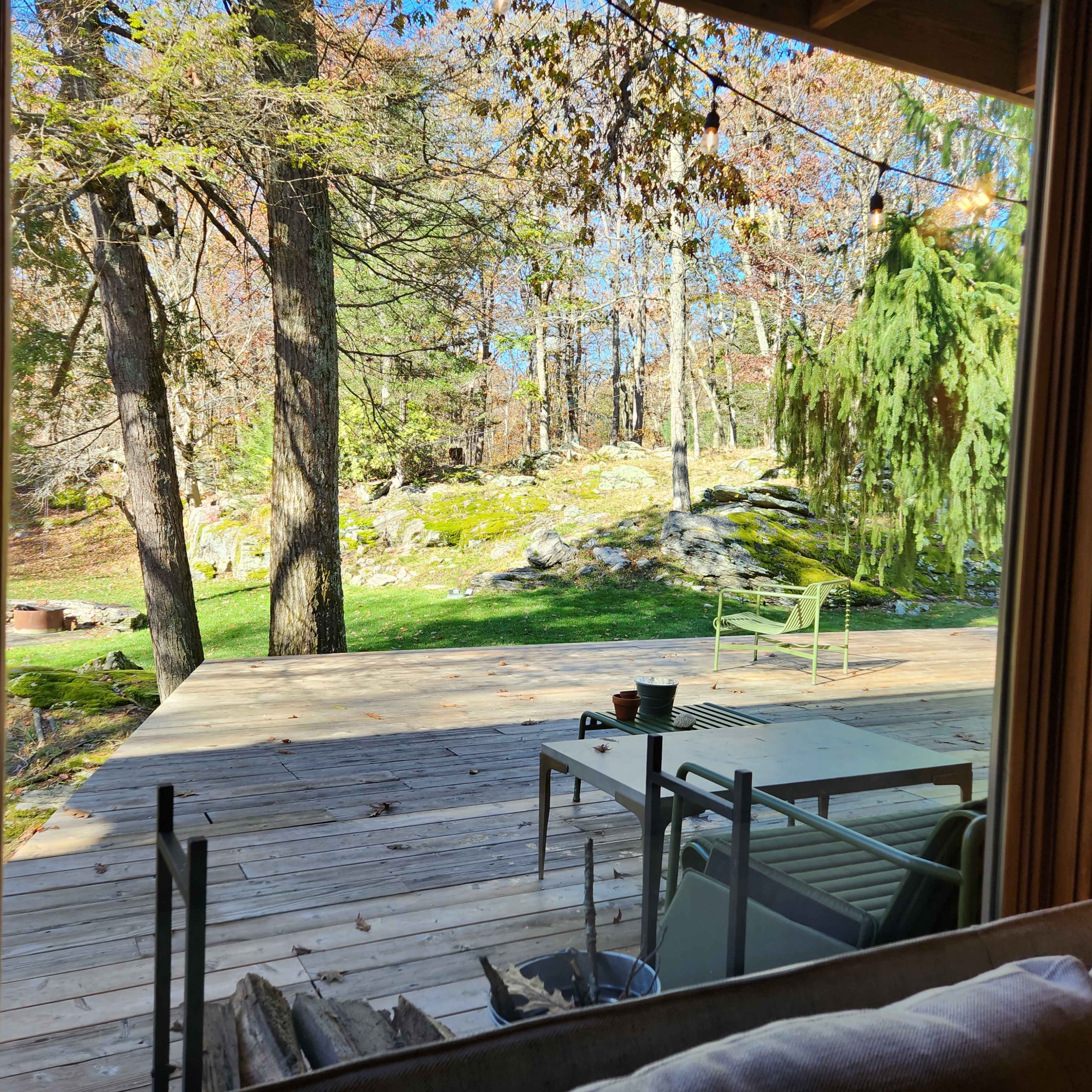 A wooden deck extends into a forested area, framed by trees and rocks, with a green chair and table visible.