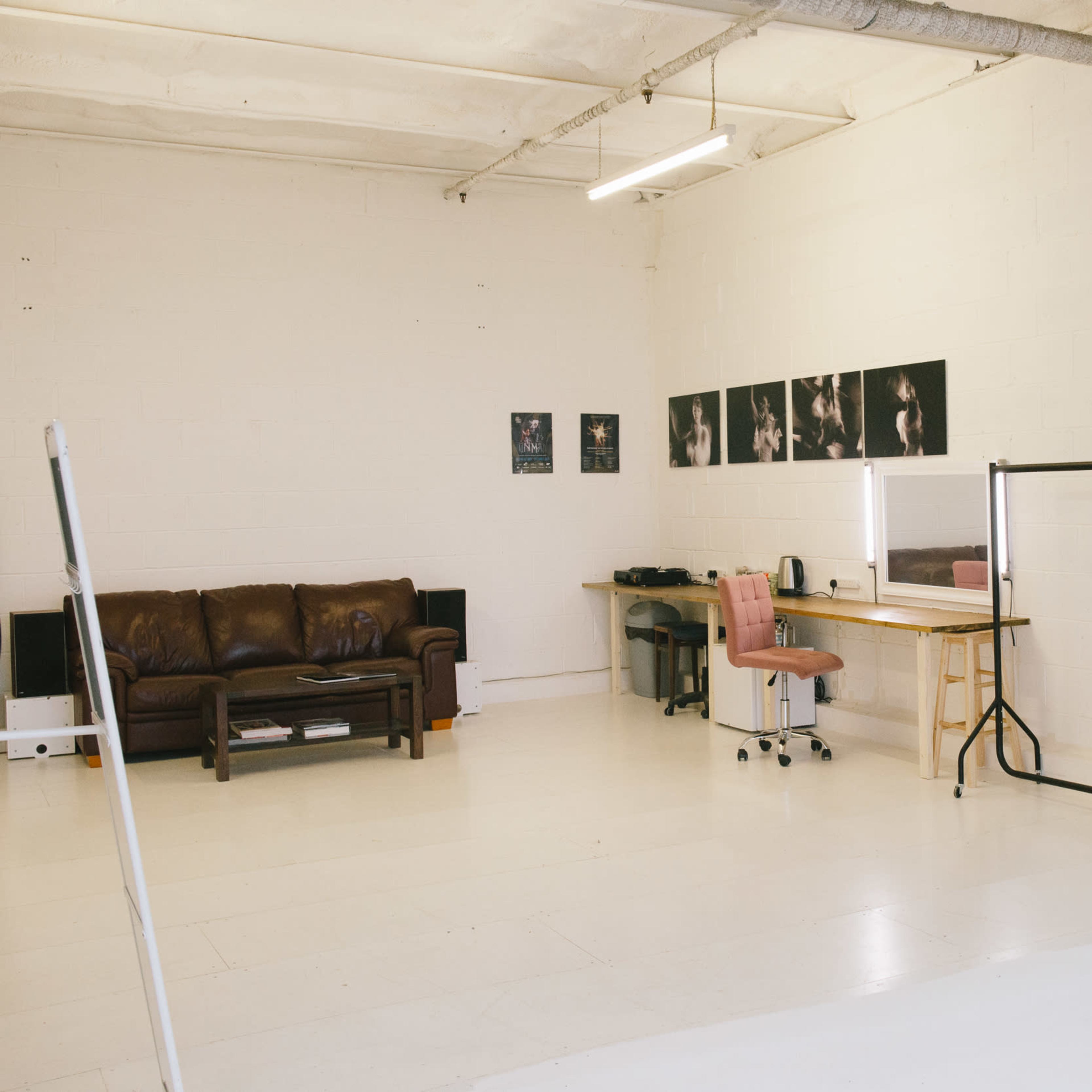 A spacious, well-lit studio with a brown leather couch, a desk with office equipment, and a clothing rack along one wall.