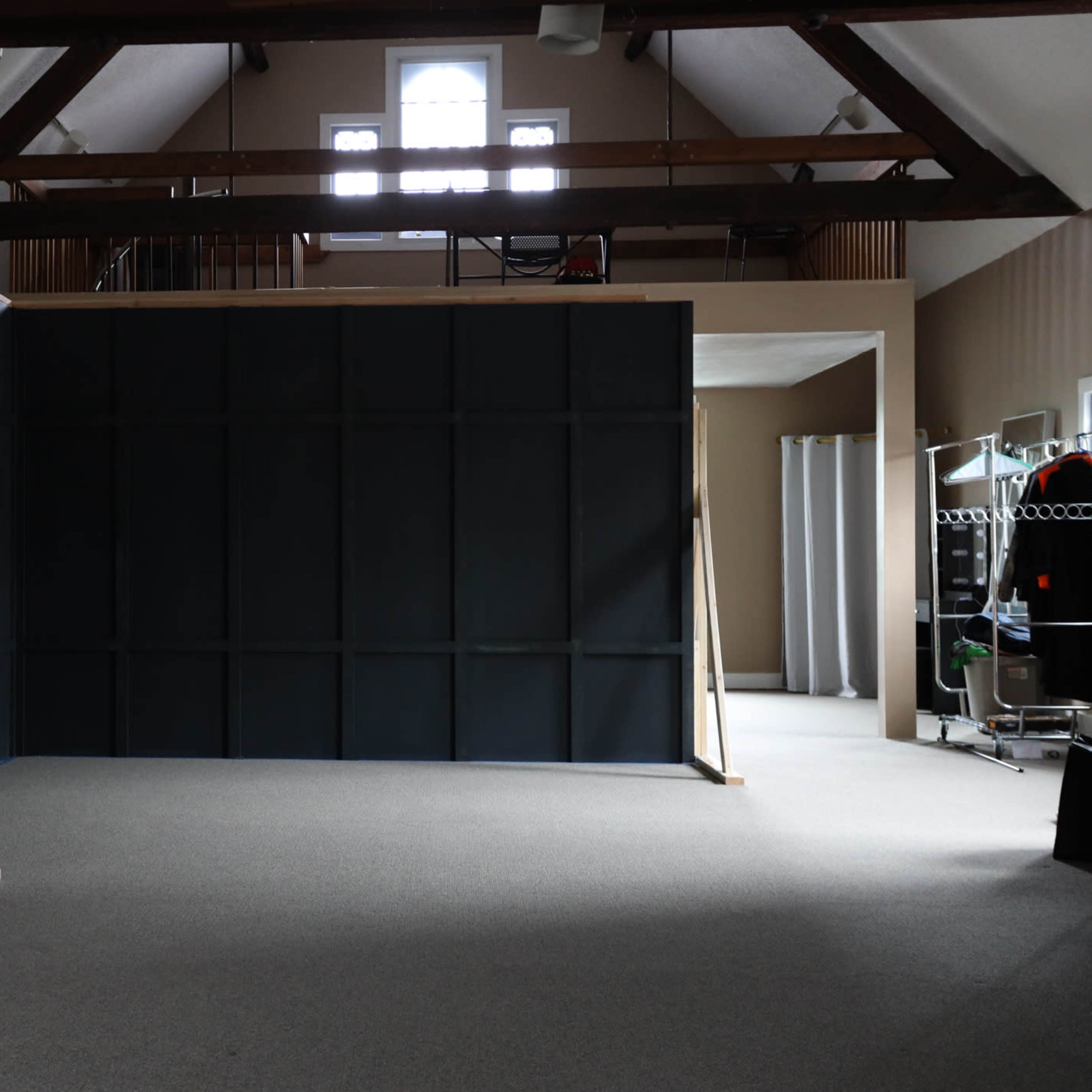 An empty room with a large dark wall structure supported by wooden beams, and a few pieces of furniture in the background.